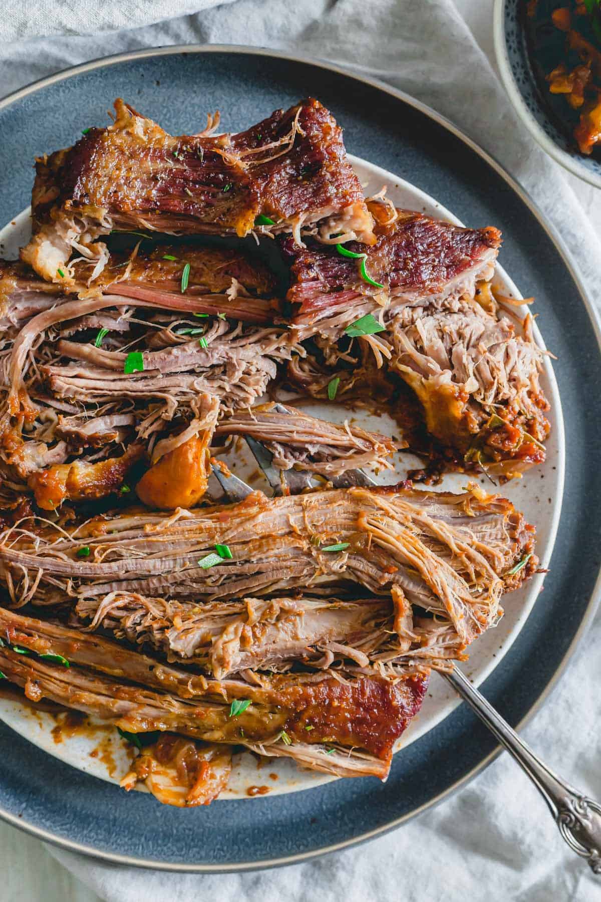 Tender braised veal brisket pulled apart into pieces on a plate with a tomato herb sauce.