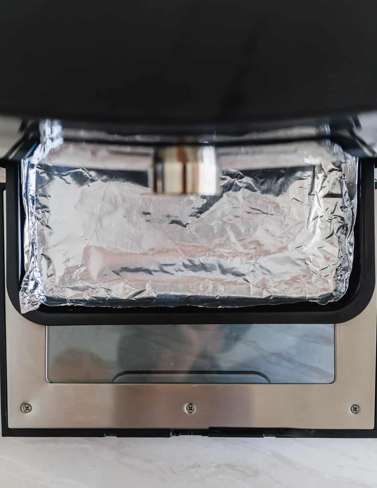 Bottom tray of an air fryer oven lined with tin foil.