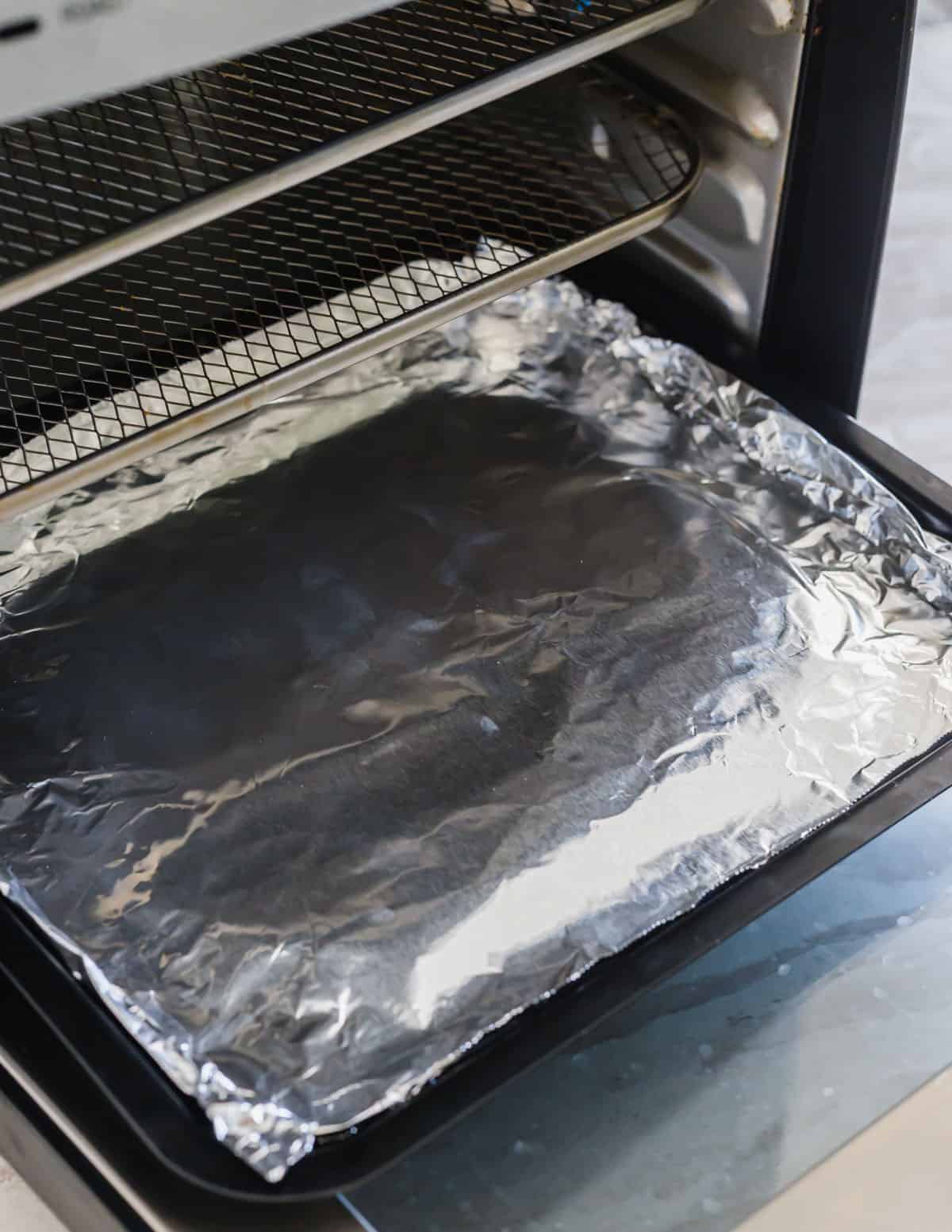 Inside of an air fryer with aluminum foil lining the bottom tray for easy clean up.