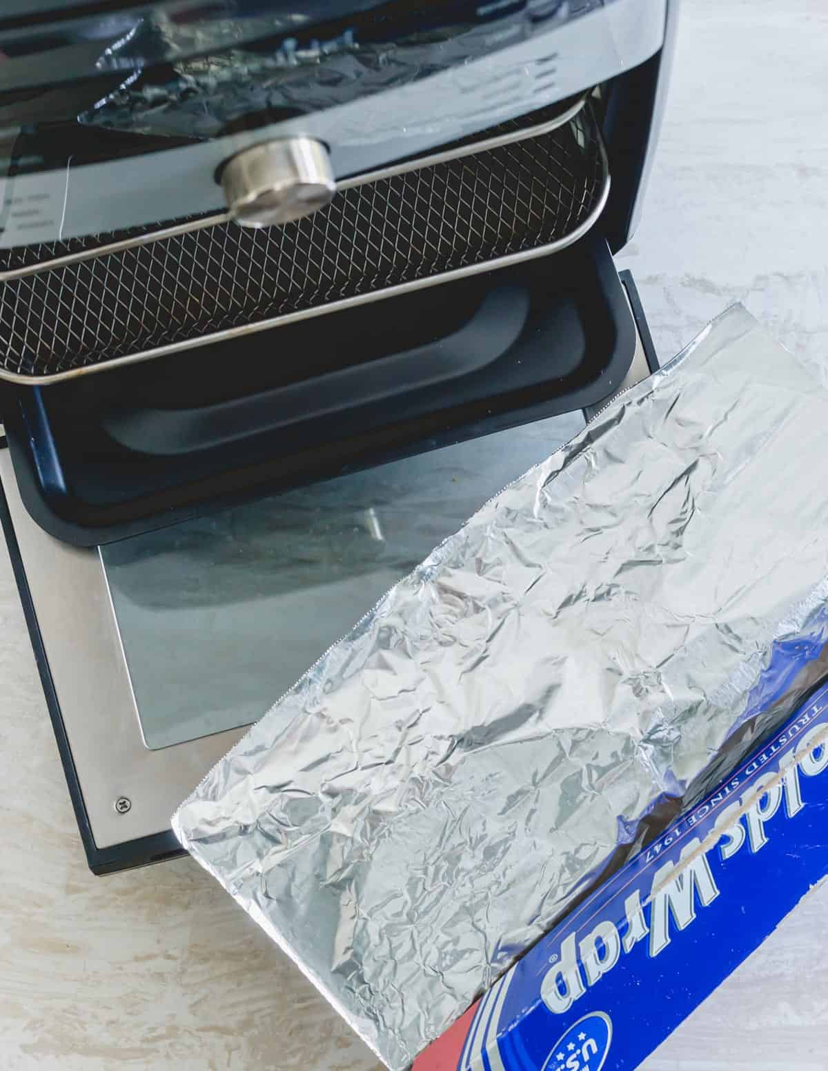 Pampered Chef deluxe air fryer with aluminum foil next to it.