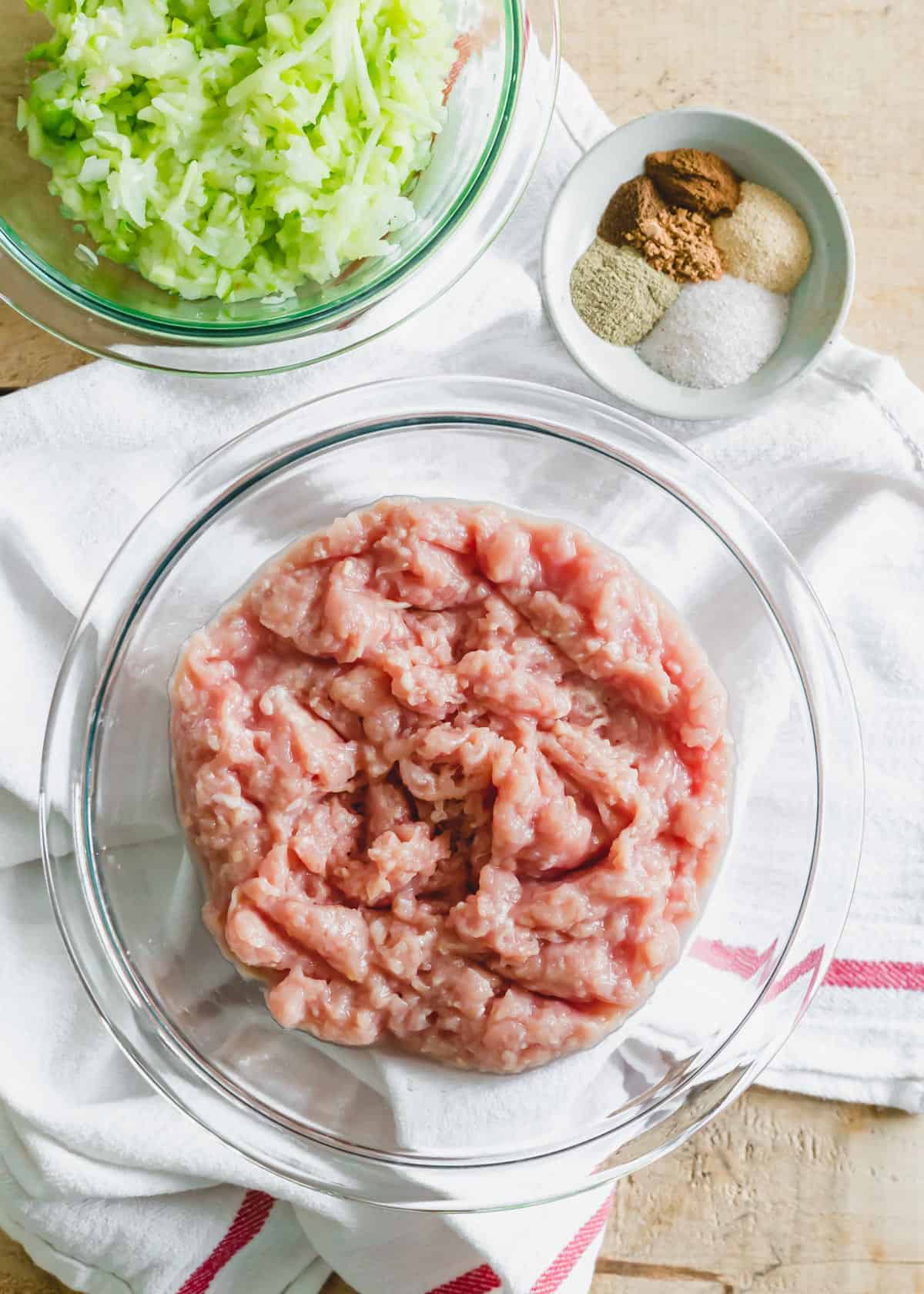 Ingredients to make chicken sausage breakfast patties including raw ground chicken, grated apples and onion and spices.