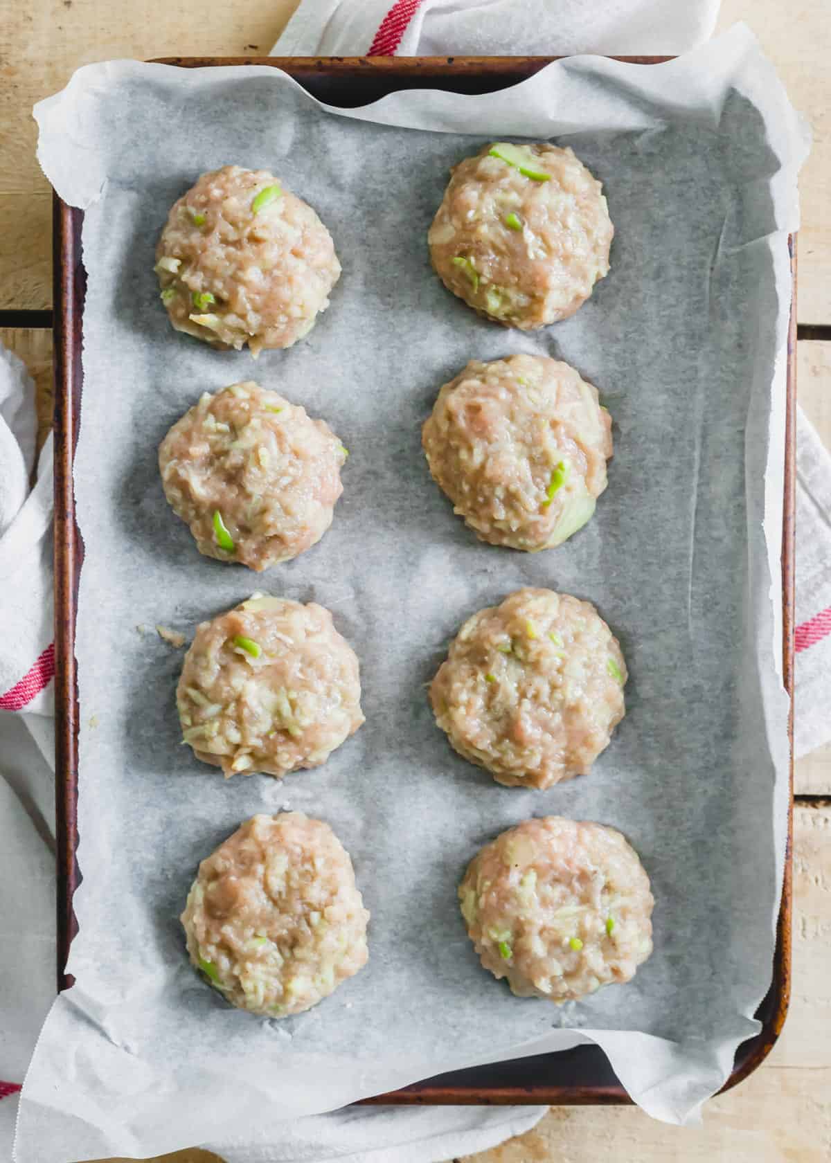 Prepared chicken sausage patties on a baking sheet lined with parchment paper.