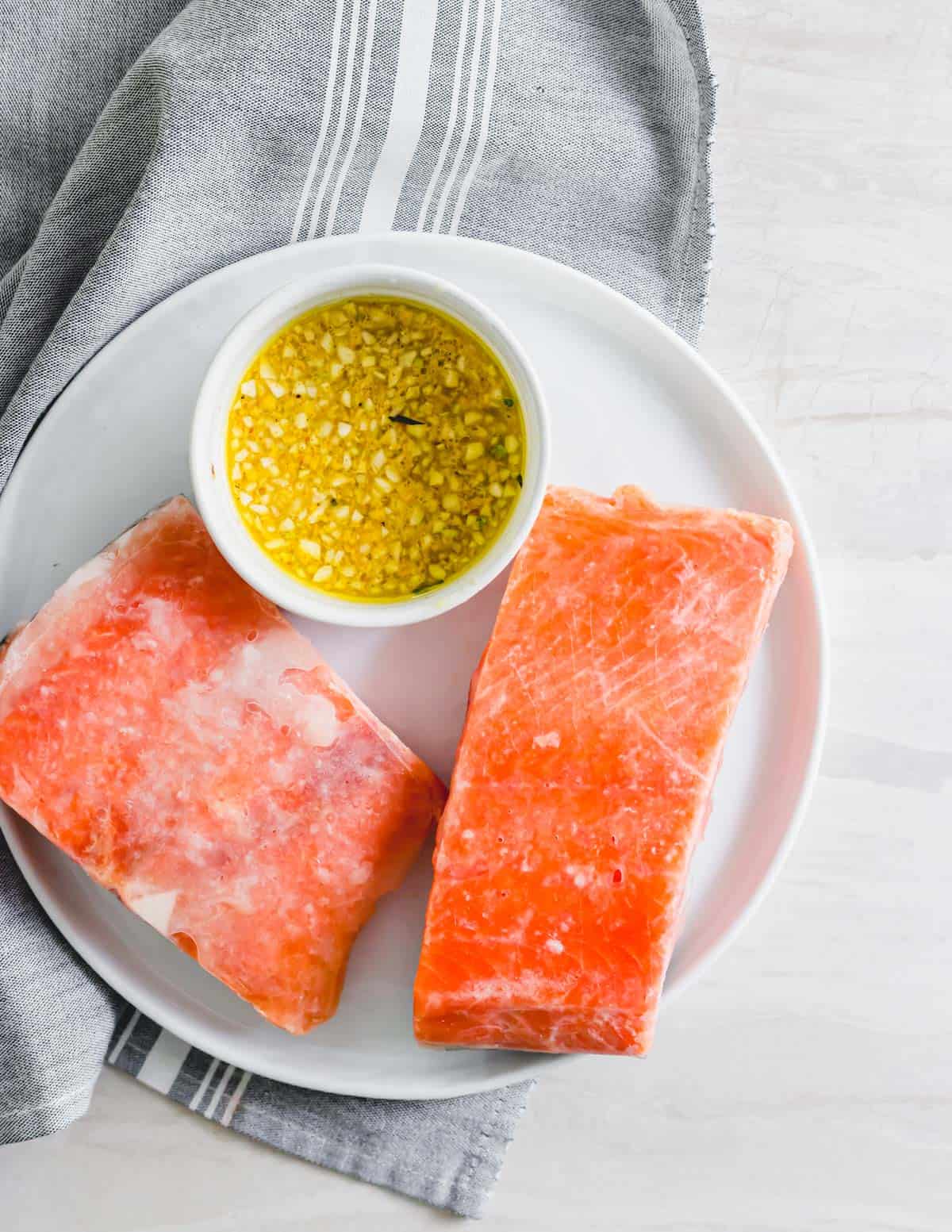 Frozen salmon filets on a white plate with maple mustard garlic sauce in a small bowl.