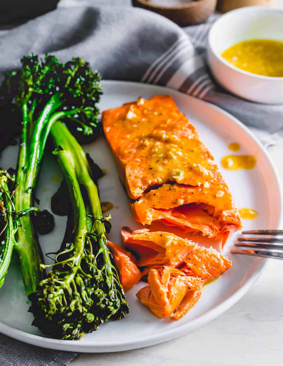 Air fryer frozen salmon on a plate with  a fork and broccolini on the side.