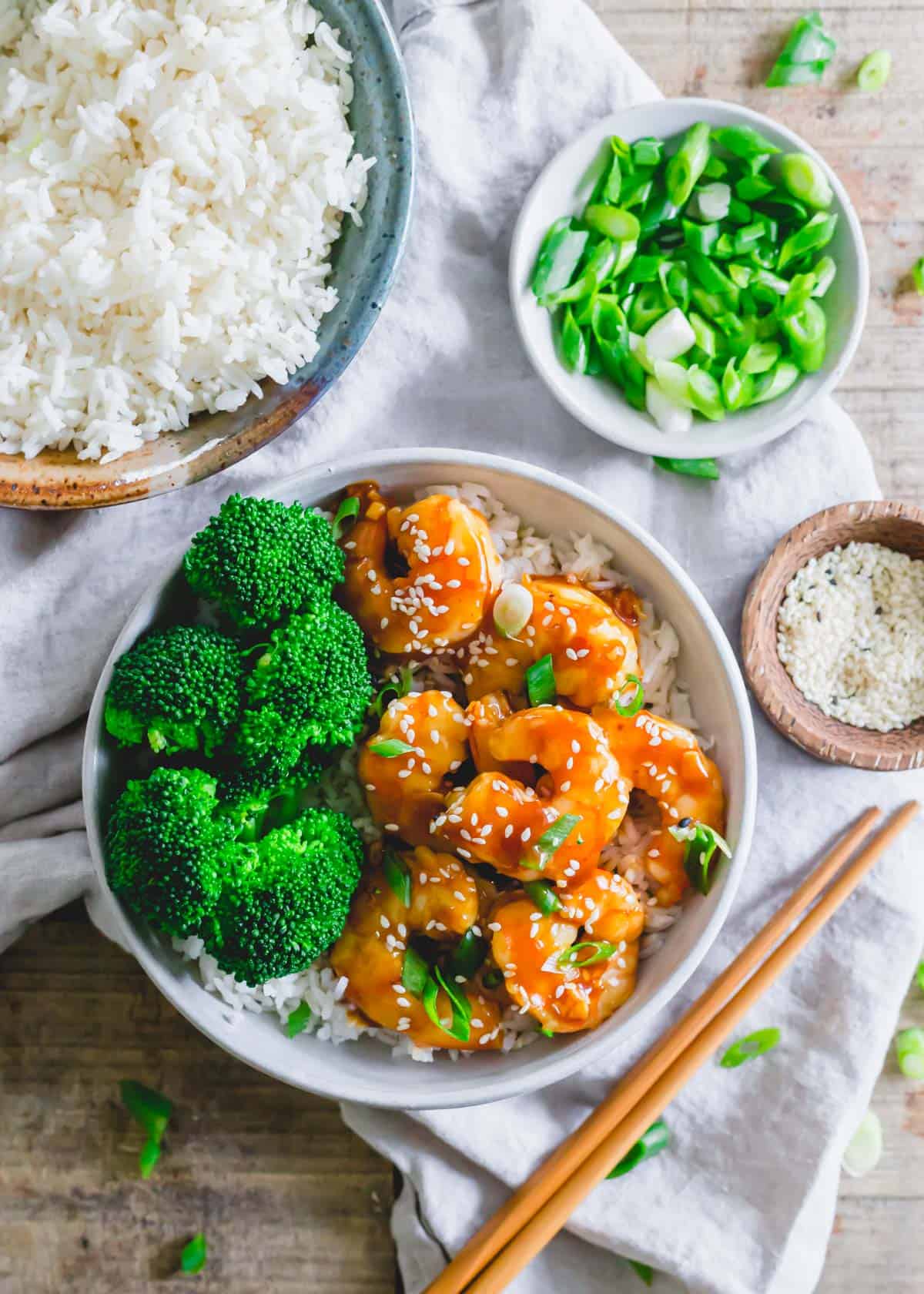 Homemade general Tso shrimp in a bowl with broccoli and white rice. Garnished with sesame seeds and scallions.