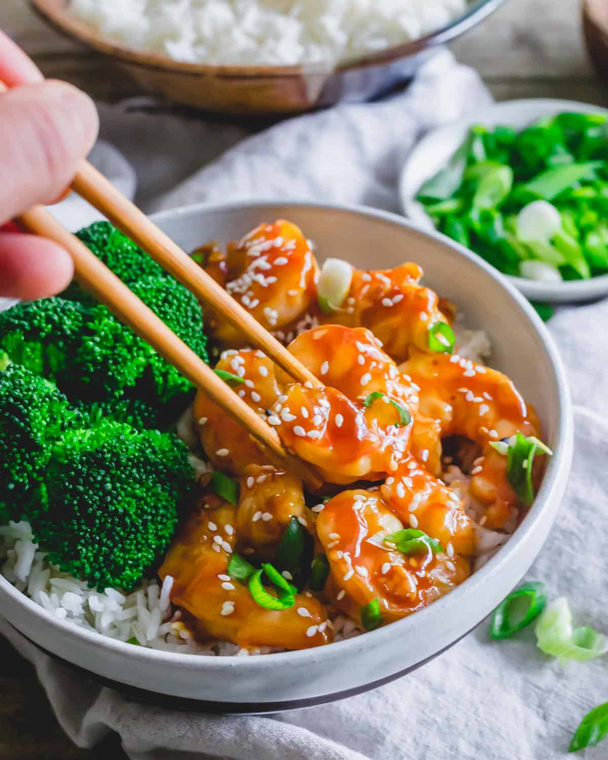 Chopsticks picking up a piece of General Tso shrimp in a bowl.