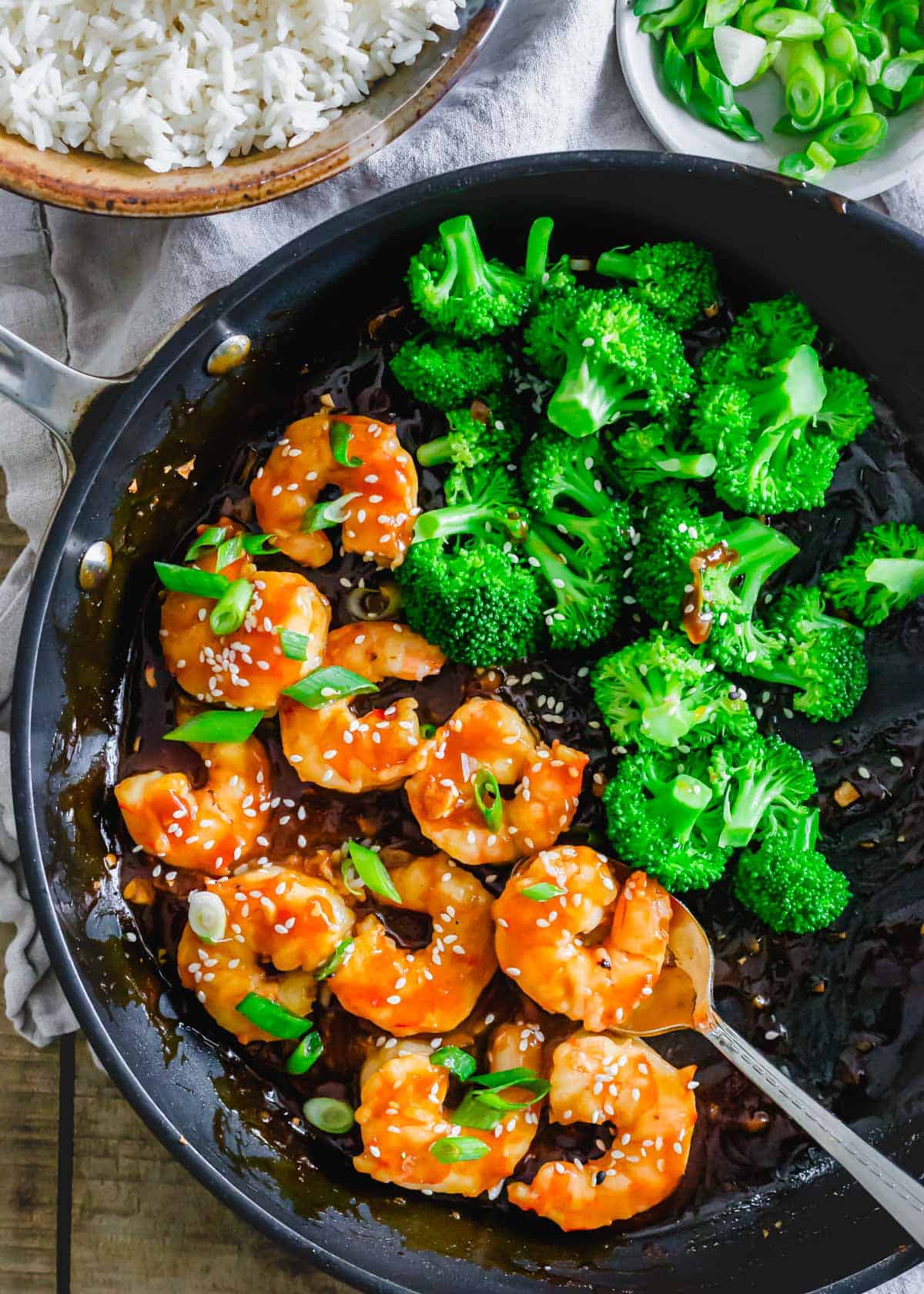 Cooked shrimp coated in General Tso's sauce with broccoli in a skillet.