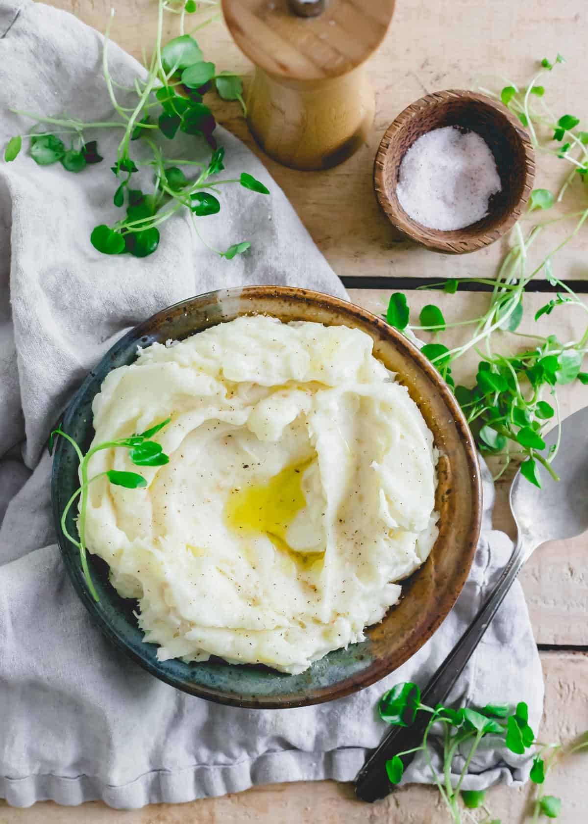 Mashed yuca root recipe in a bowl garnished with baby greens. Salt and pepper on the side.