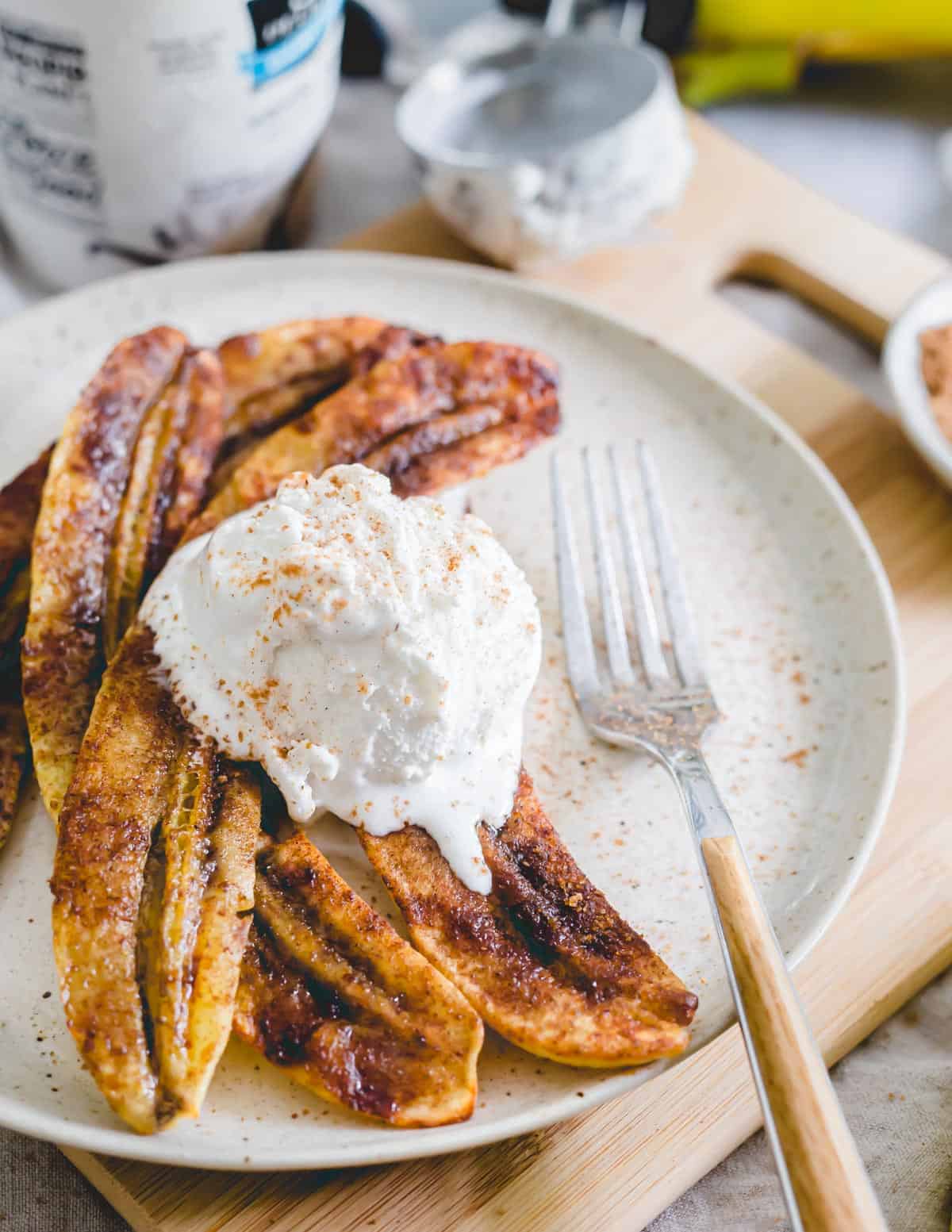 Air fryer bananas on a plate with vanilla ice cream and a fork.
