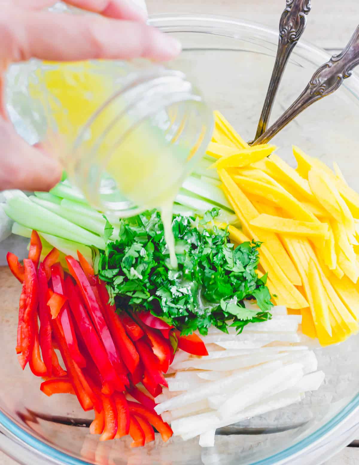 Honey lime dressing in a mason jar poured over jicama salad ingredients in a large bowl.