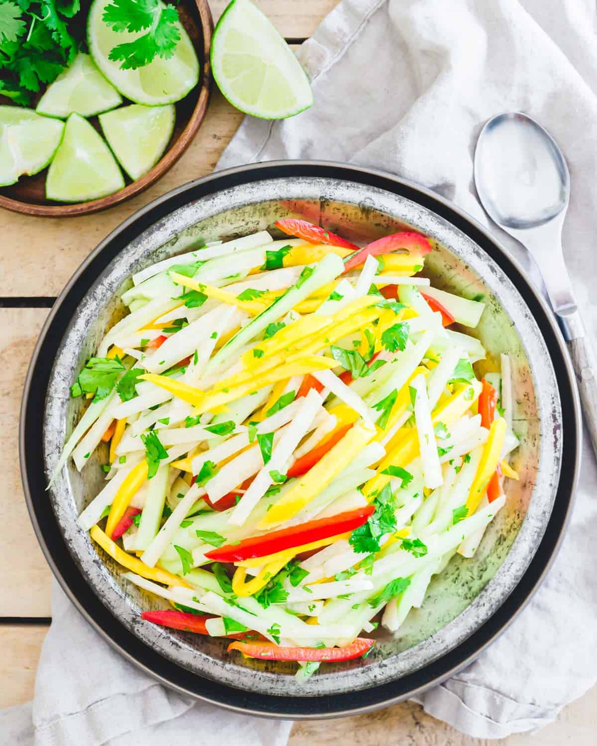 Jicama mango salad in metal dish with lime and cilantro on the side.