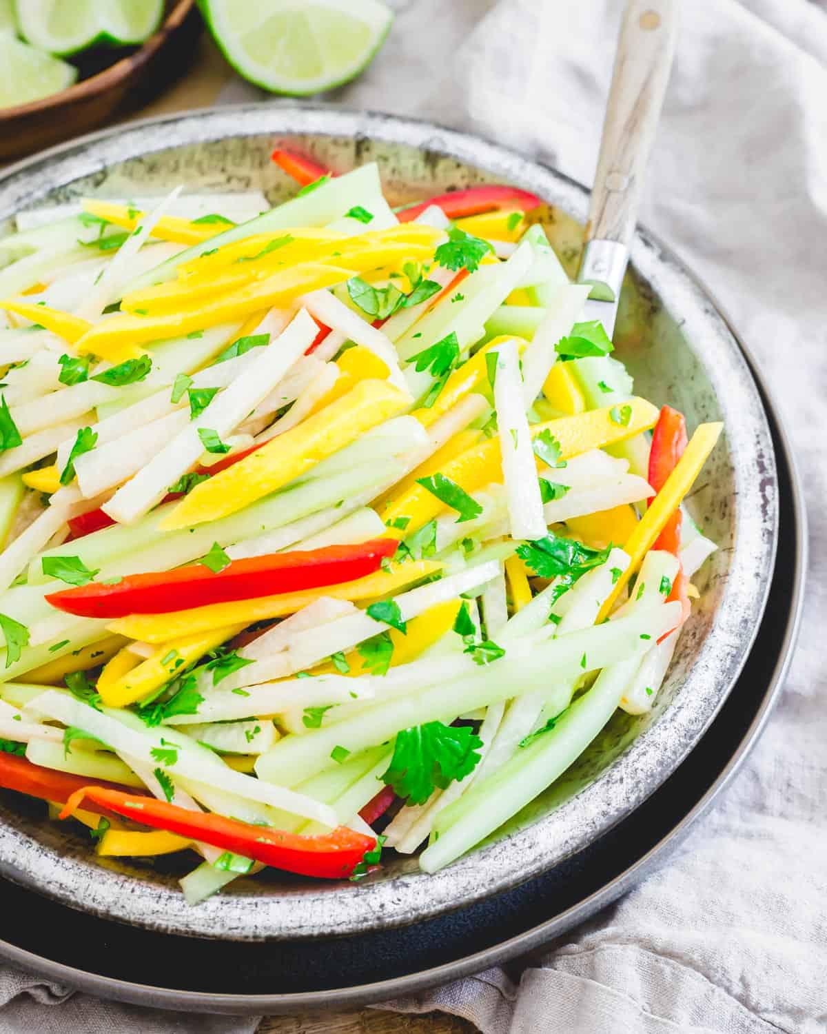 Refreshing and healthy jicama salad recipe in a metal bowl garnished with cilantro with a serving spoon.