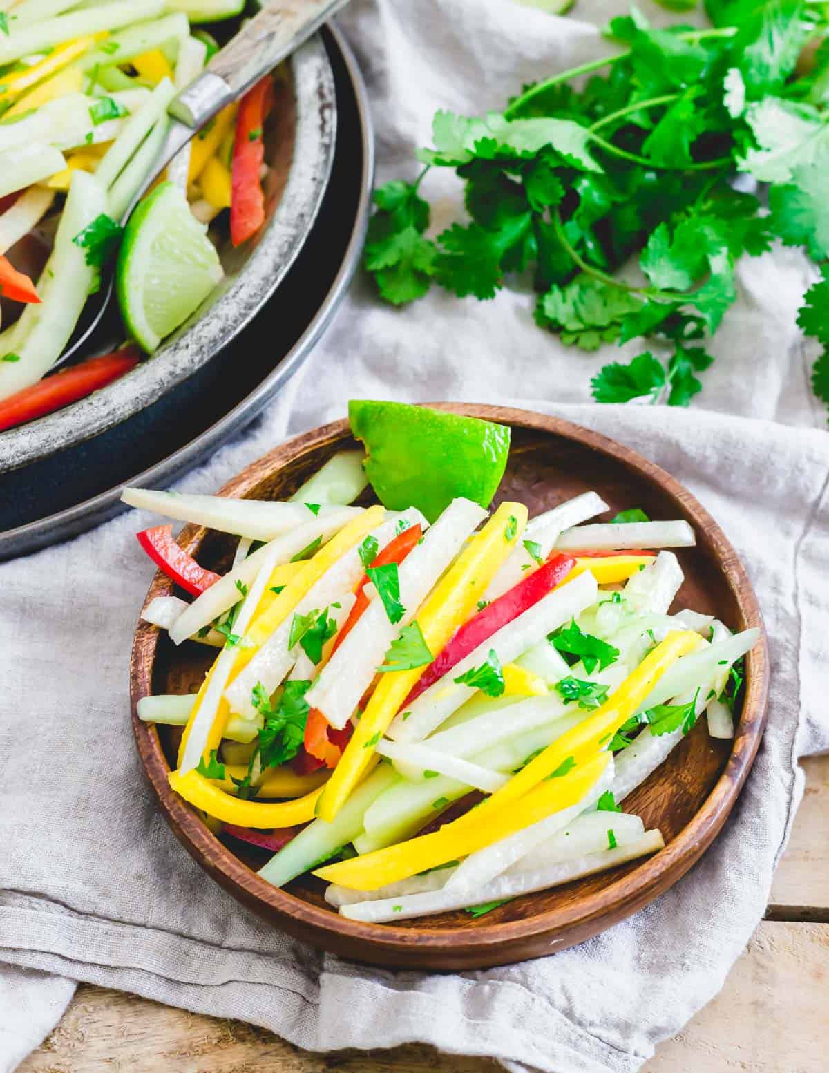 Jicama salad with honey lime dressing on a small wooden plate with a lime wedge.