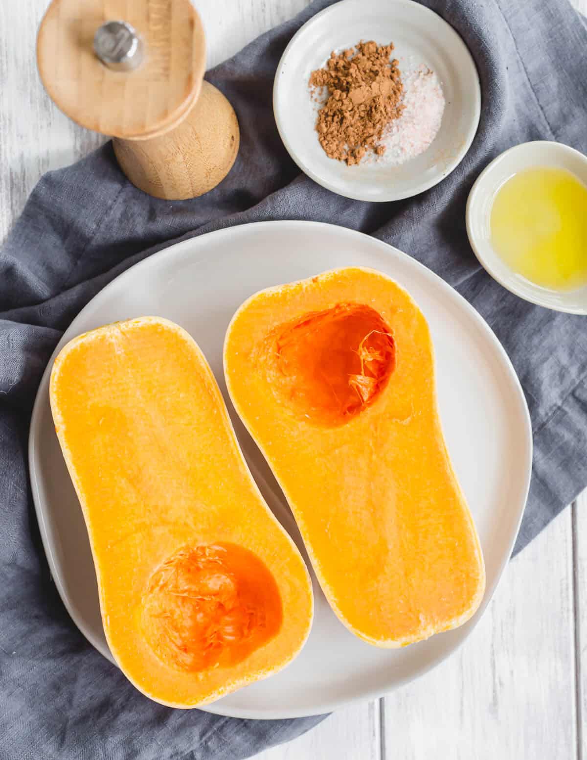 Halved and seeded butternut squash on a plate with melted ghee and seasonings on the side.