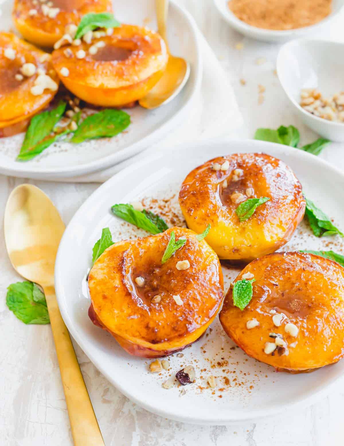 Air fryer peaches topped with cinnamon sugar, chopped walnuts and fresh mint on a white plate.