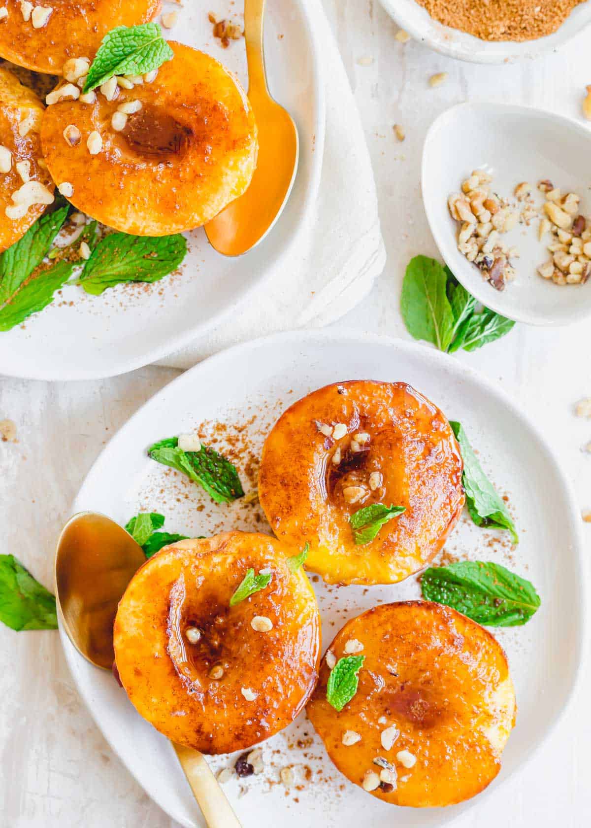 Caramelized cinnamon sugar peaches made in the air fryer garnished with chopped nuts and mint on a plate.
