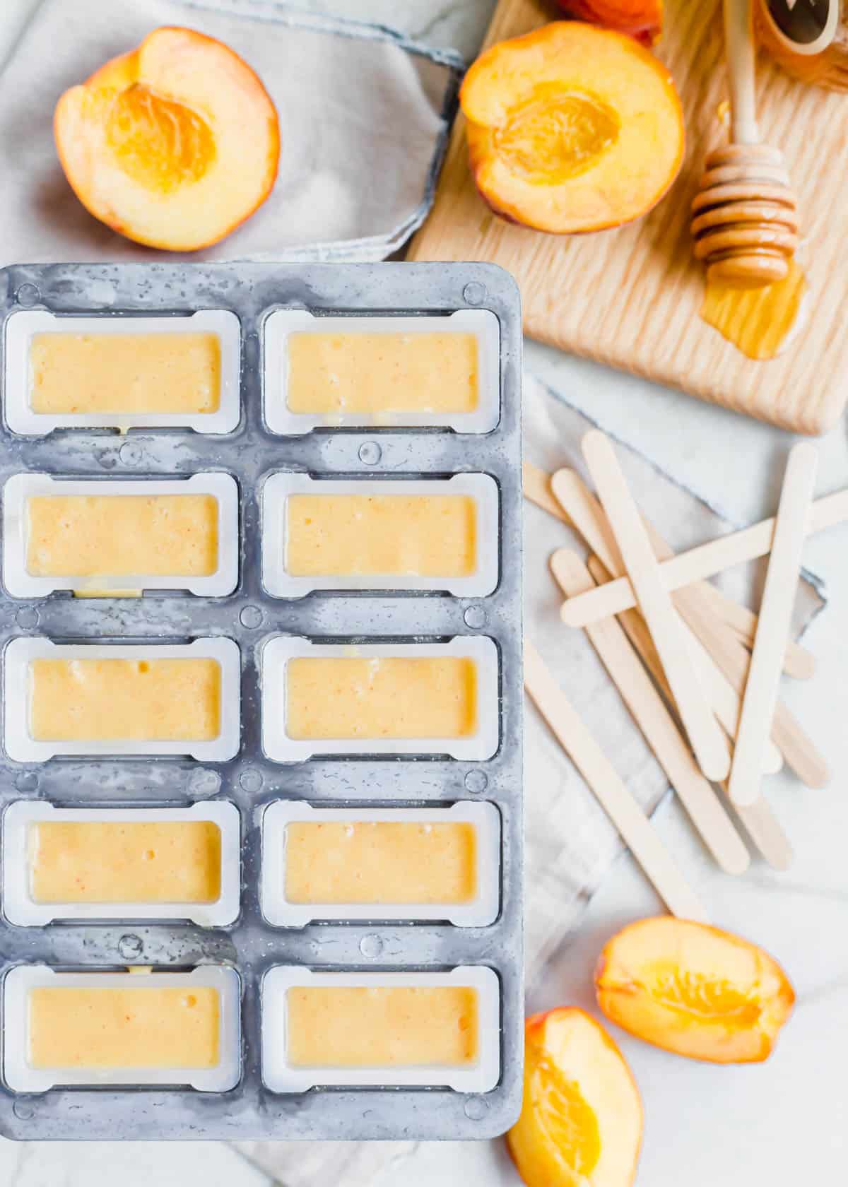 A popsicle mold filled with creamy peach filling with ice pop sticks on the side.