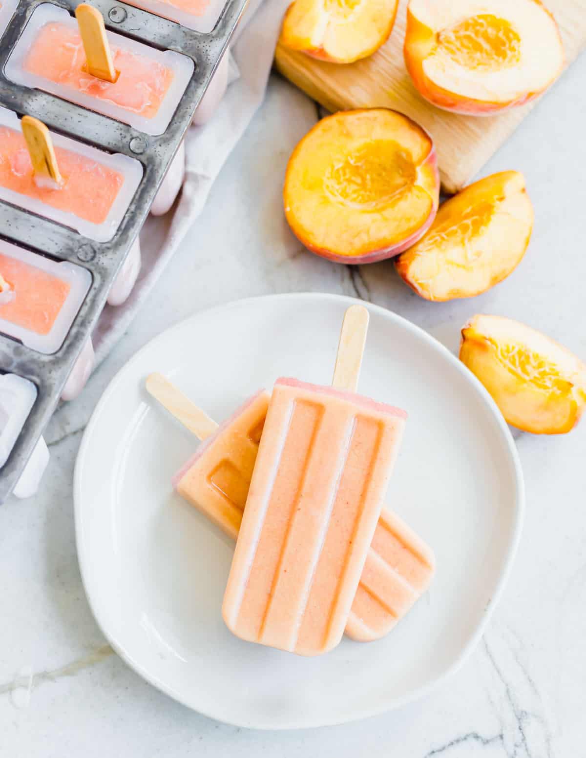 Two creamy peach ice pops stacked on top of each other on a white plate.