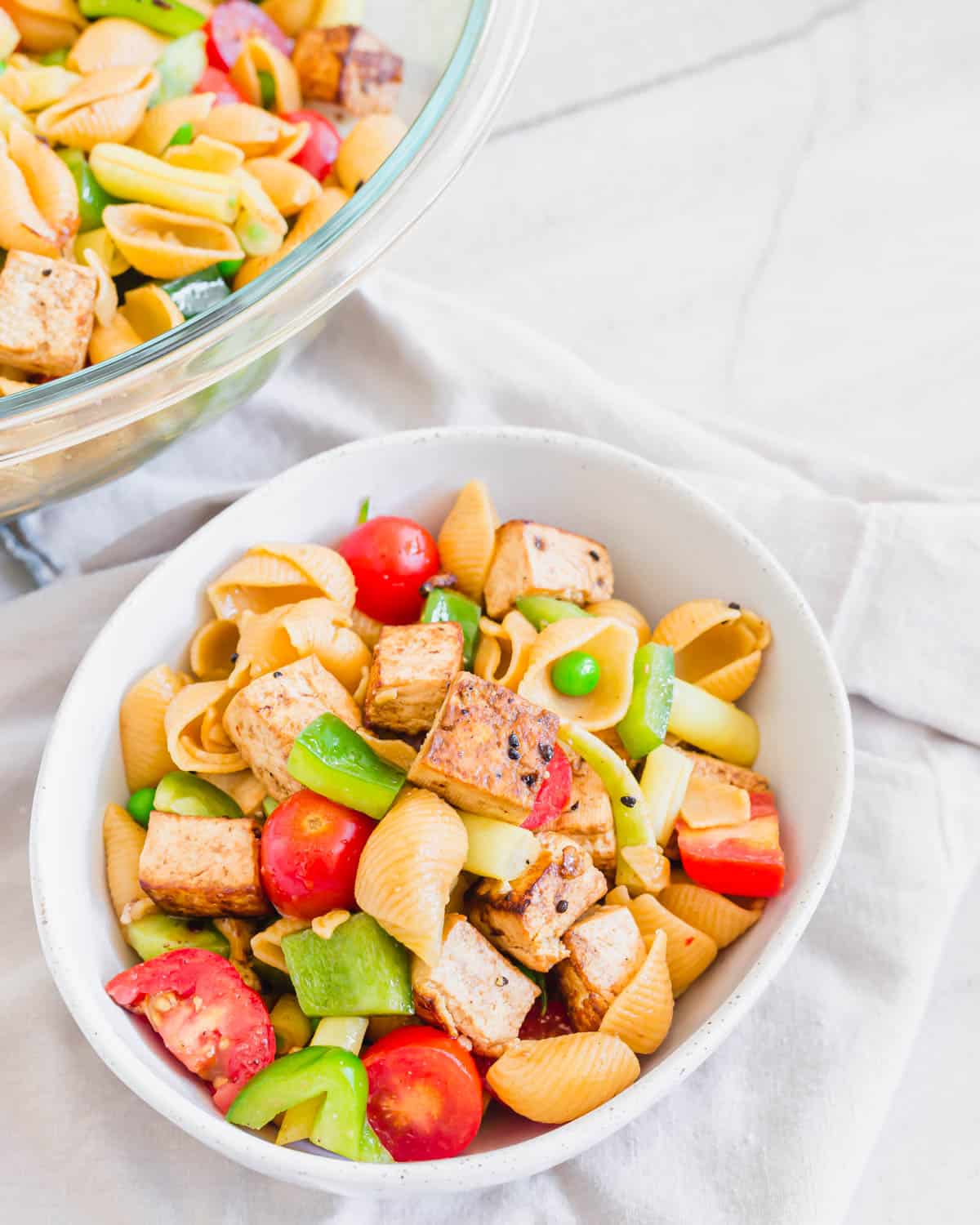 A healthy and easy tofu pasta salad recipe in a white bowl with a larger bowl in the background.