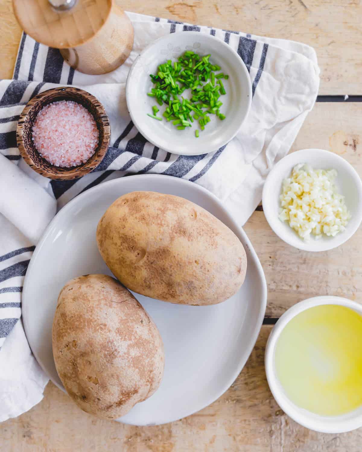 Ingredients to make hasselback potatoes in the air fryer: russet potatoes, ghee, minced garlic, fresh chives, salt and pepper.