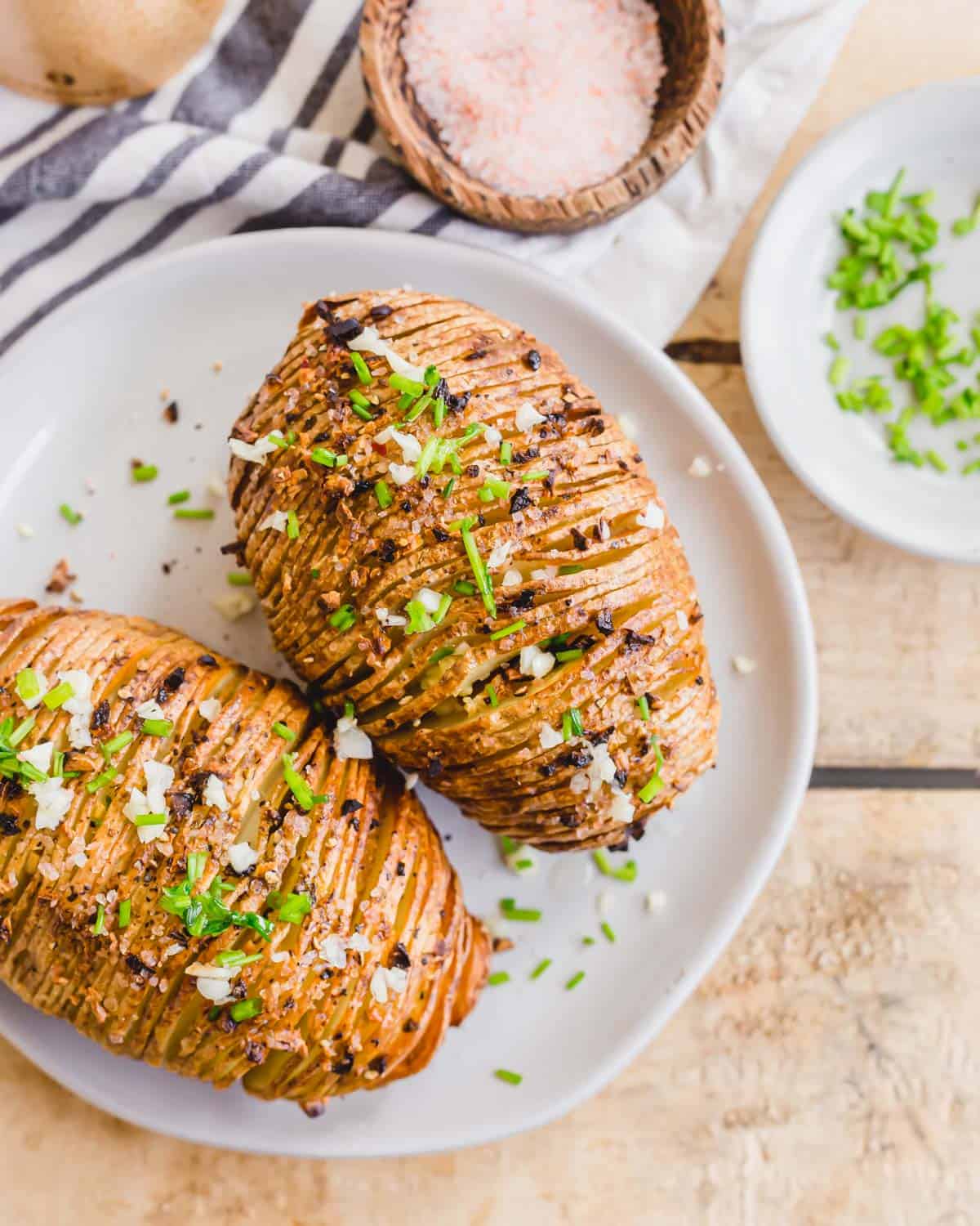 Air fried hasselback potatoes on a plate with garlic and fresh chives.
