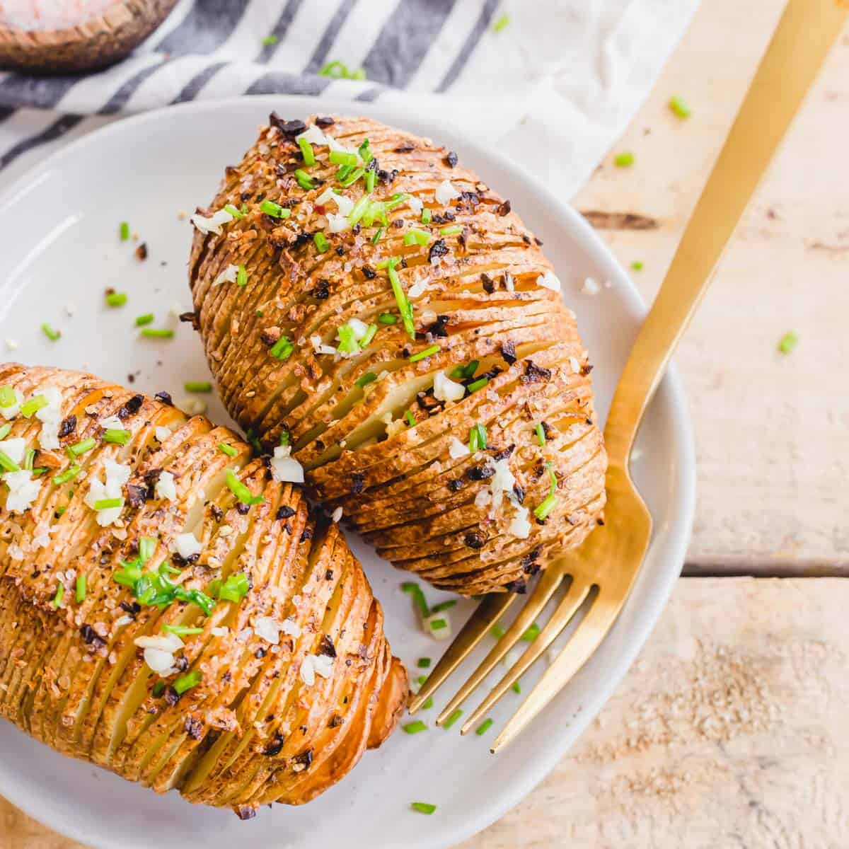 Air fryer hasselback potatoes on a plate garnished with garlic and chives with a fork on the side.