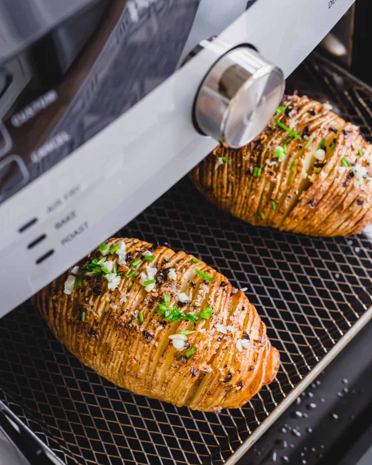 Hasselback white potatoes on an air fryer tray garnished with chives.