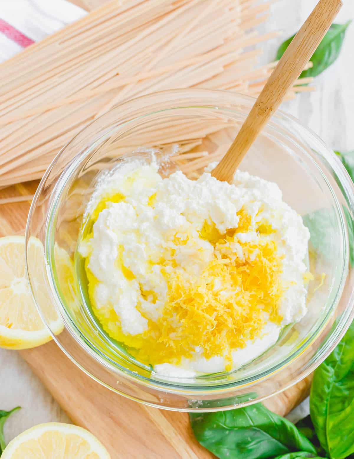Making lemon ricotta sauce in a glass bowl with fresh lemon and basil on the side.