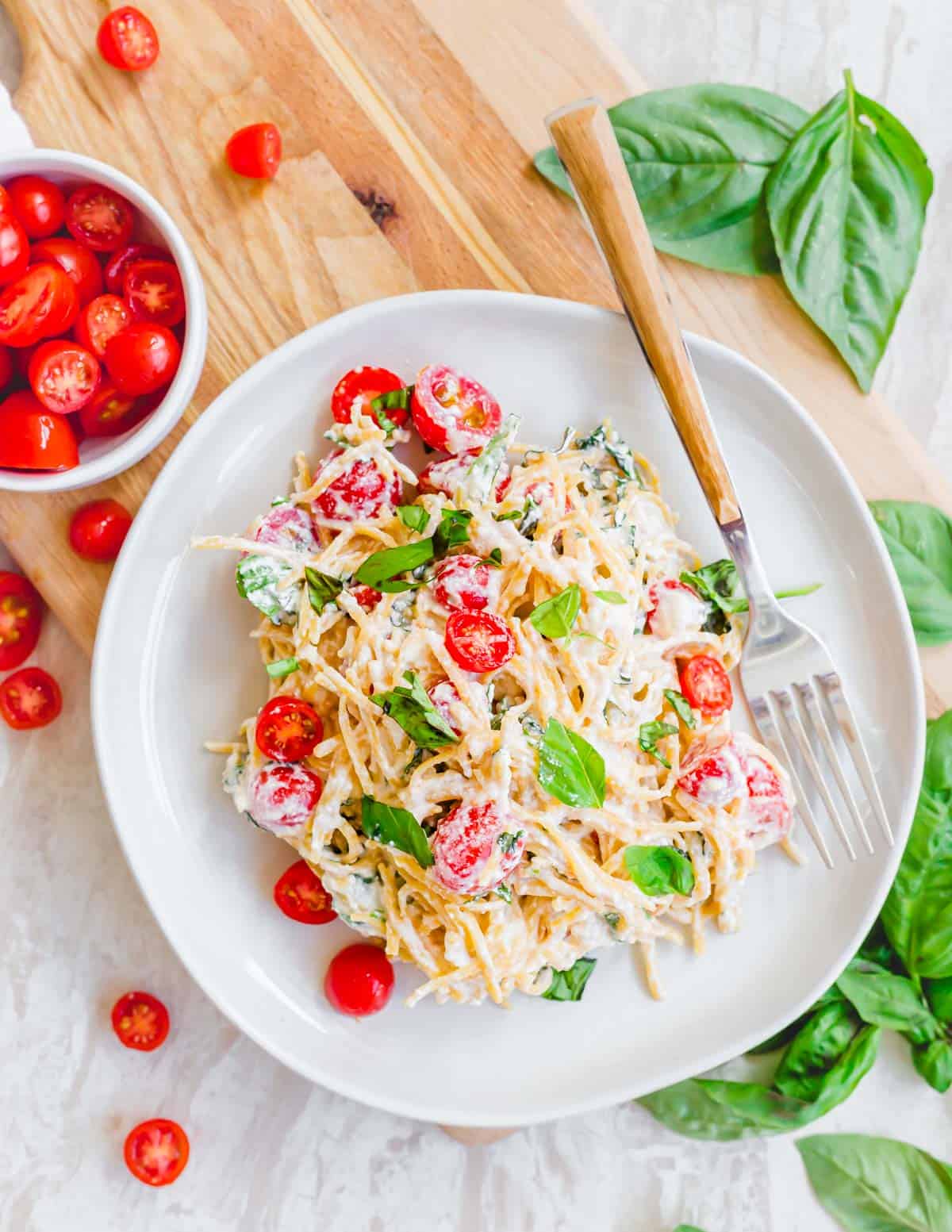 Lemon ricotta pasta on a white plate with a fork and cherry tomatoes and fresh basil on the side.