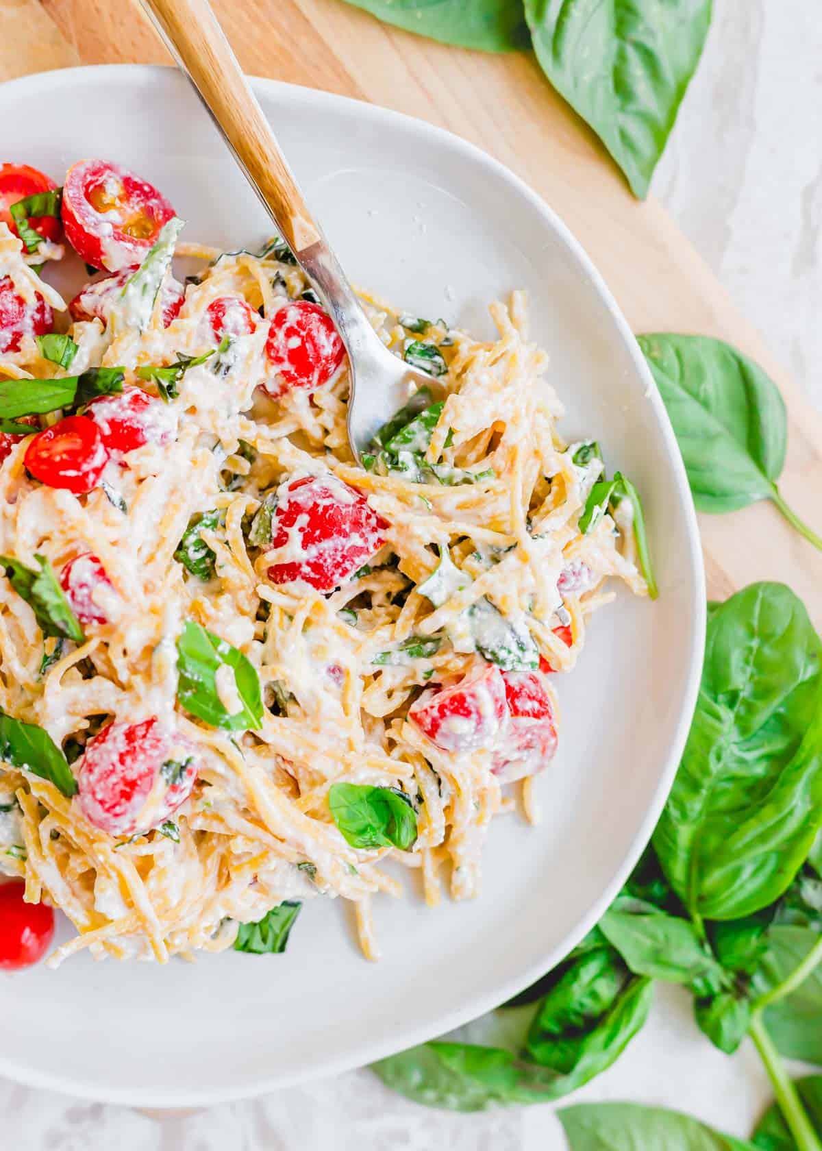 Lemon and ricotta pasta recipe with tomatoes and basil twirled on a fork on a white plate.