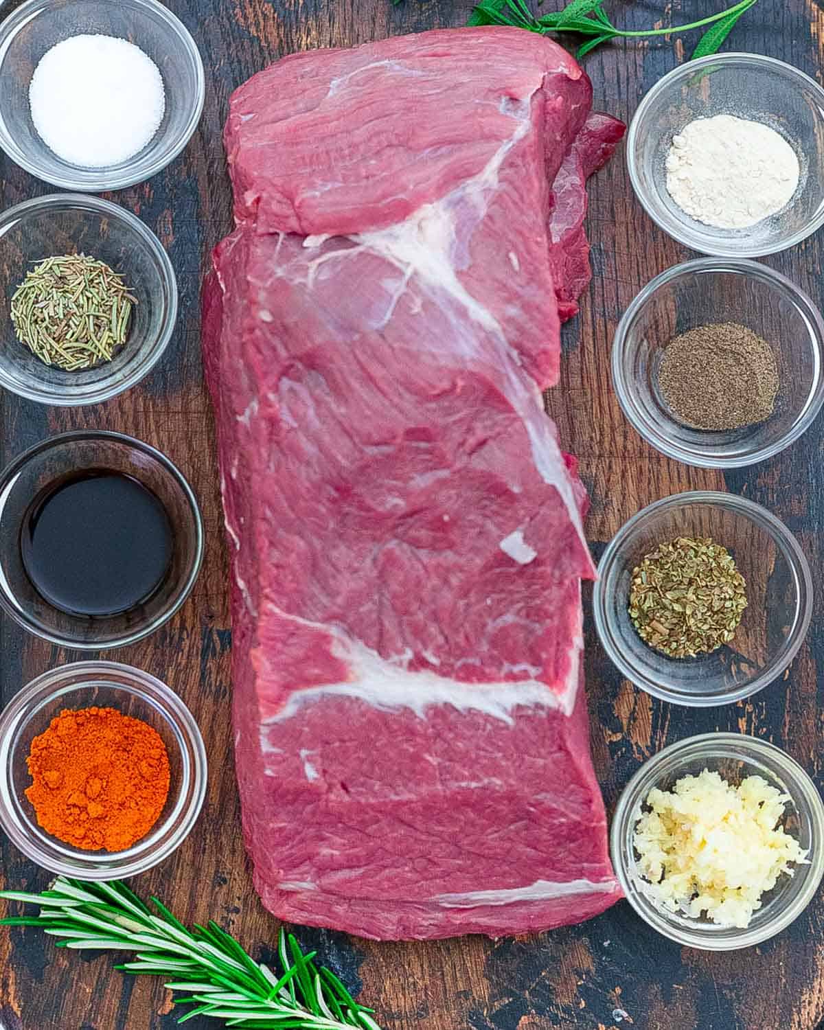 Tri tip roast on a cutting board with seasonings and ingredients to make in the slow cooker.
