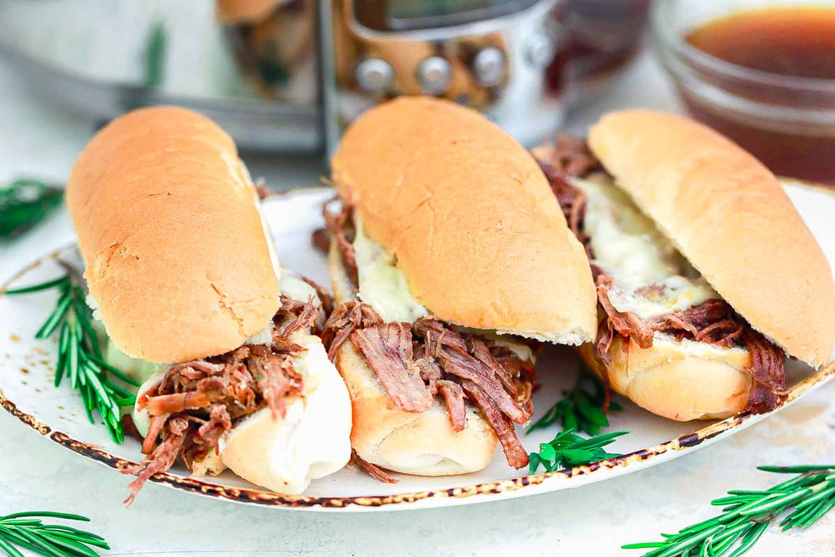 Tri tip sandwiches with melted Swiss cheese on a platter with fresh rosemary sprigs.