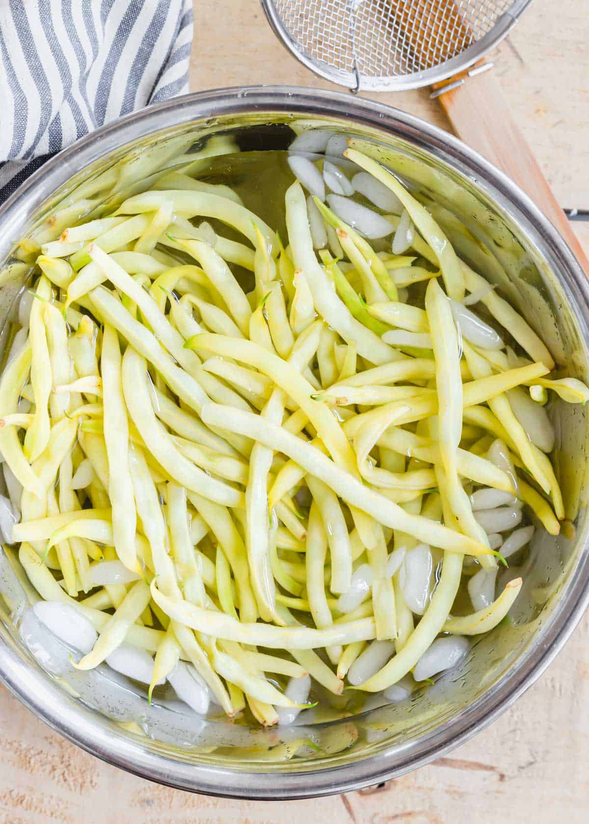 Blanched wax beans in a metal bowl with ice water.