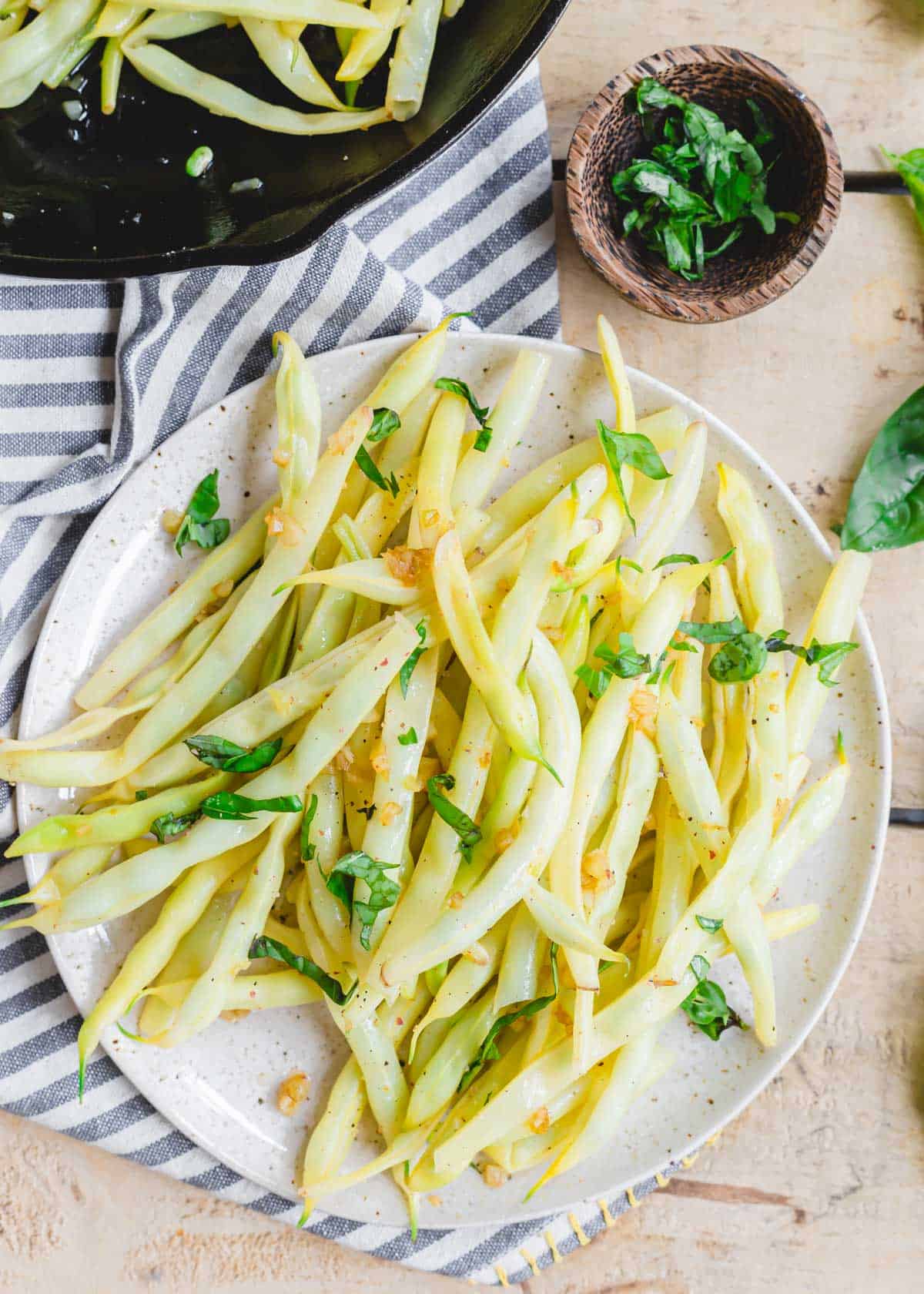 Wax beans on a plate with sautéed garlic and fresh basil.