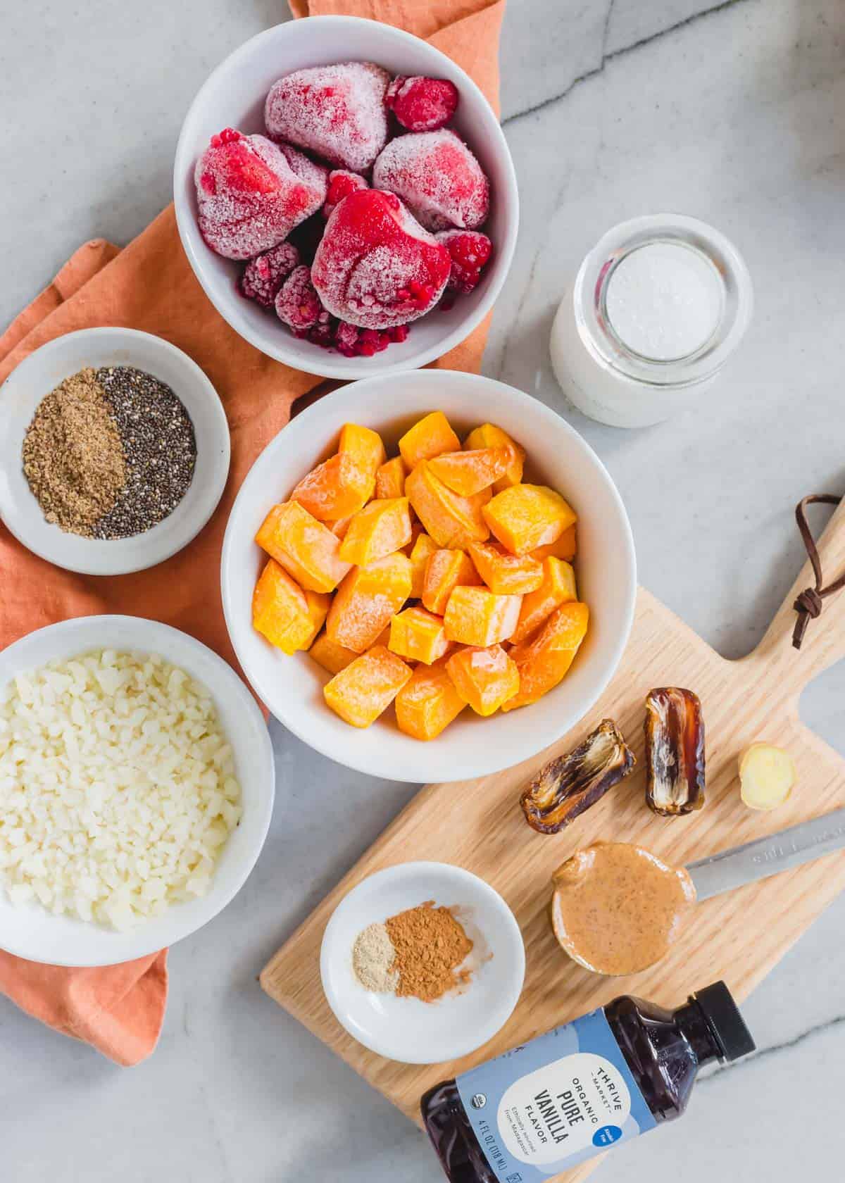 Ingredients to make a butternut squash smoothie including frozen butternut squash, frozen strawberries, frozen riced cauliflower, chia seeds, flax, almond butter, spices and vanilla.