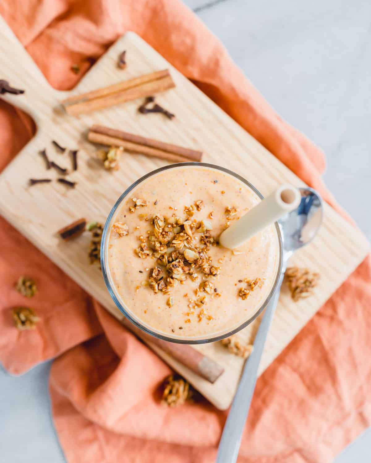 Overhead view of a butternut squash smoothie in a glass sitting on a cutting board with an orange kitchen towel.