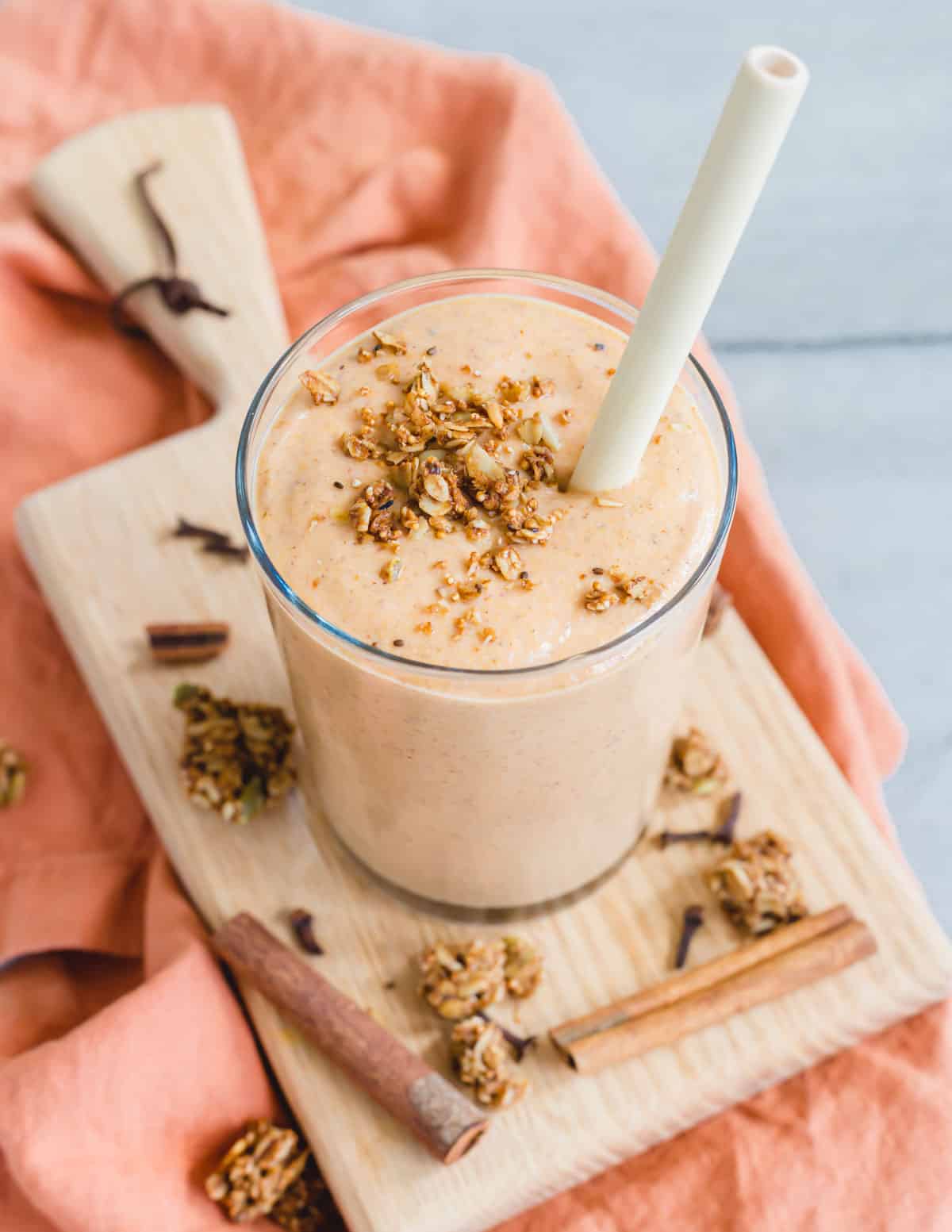 Butternut squash smoothie in a glass with a wooden straw and granola sprinkled on top.
