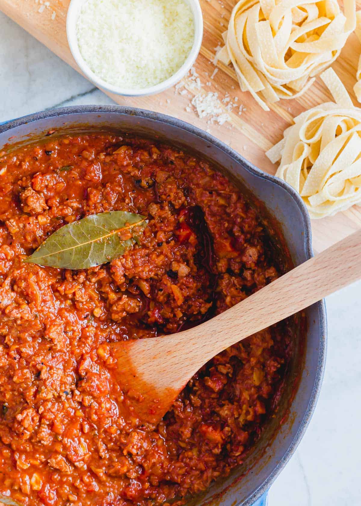 Lamb bolognese meat sauce in a Dutch oven with a wooden spoon.