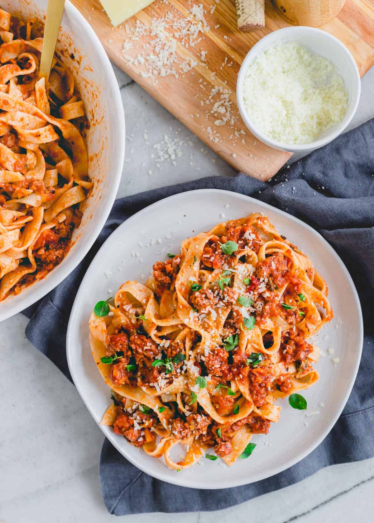 A plate of lamb bolognese tossed with fresh pasta noodles and garnished with pecorino romano and fresh oregano.