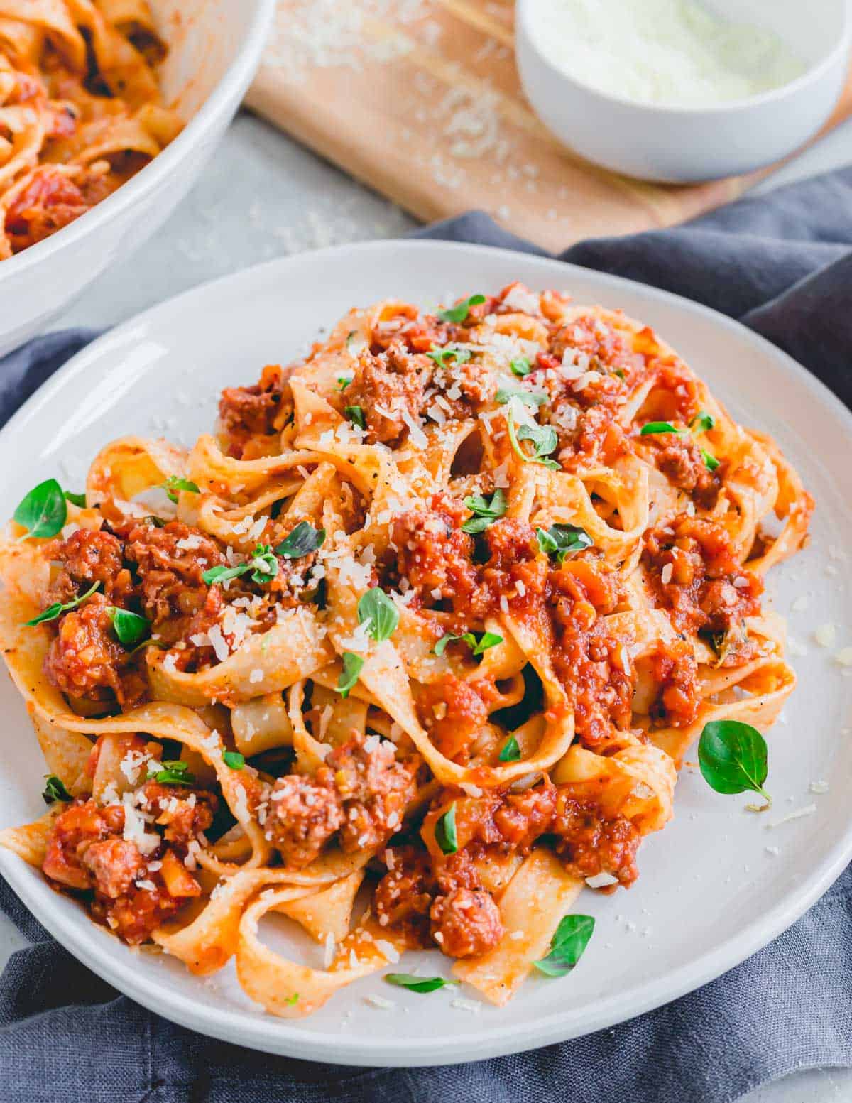 Lamb bolognese tossed with tagliatelle and fresh pecorino on a white plate.