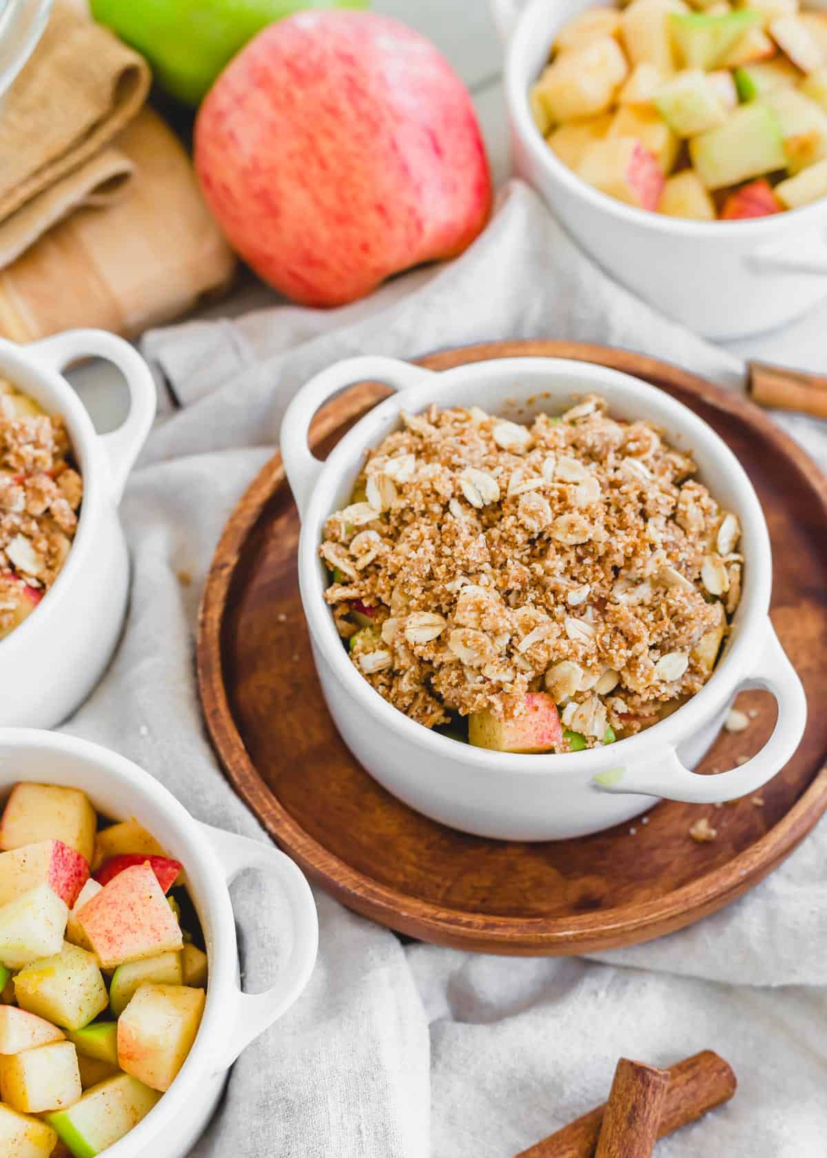 Assembling air fryer apple crisp in small white baking dishes.