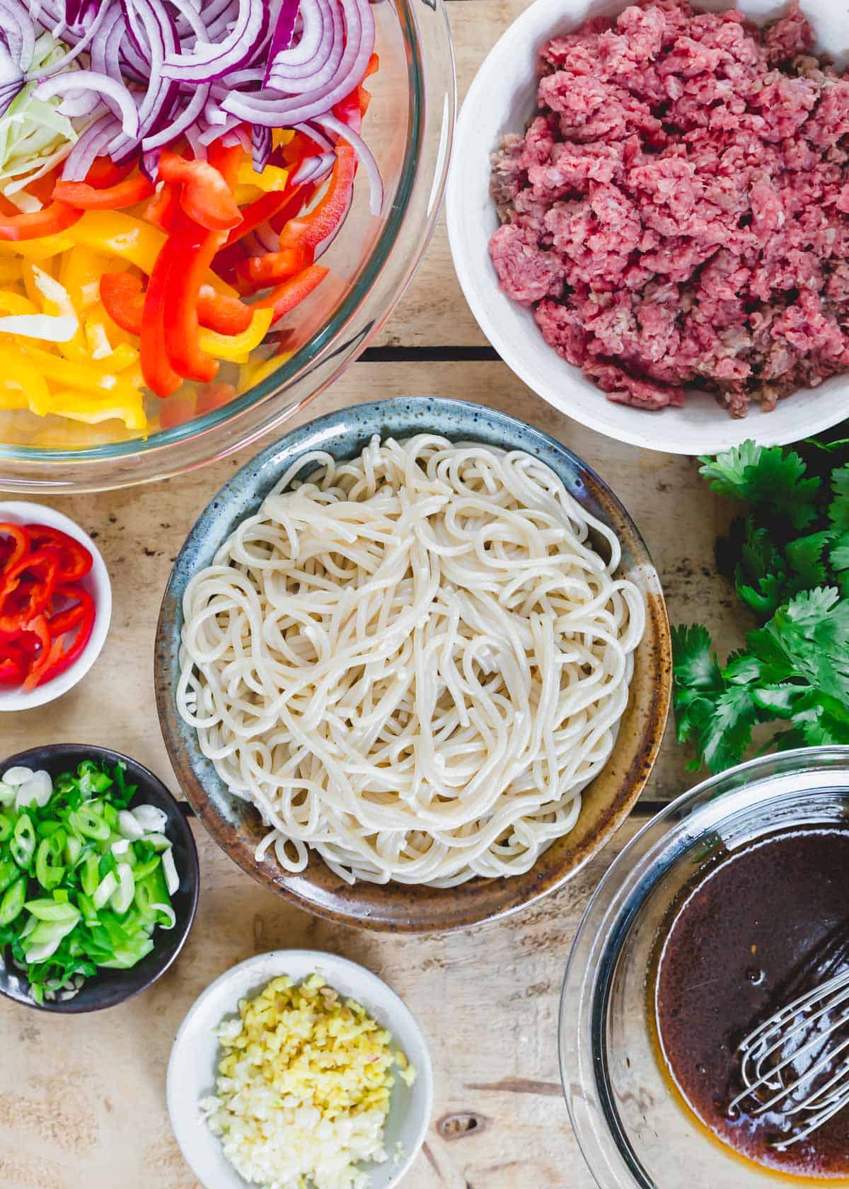 Ingredients to make spicy beef udon noodles in different bowls on a wood table.
