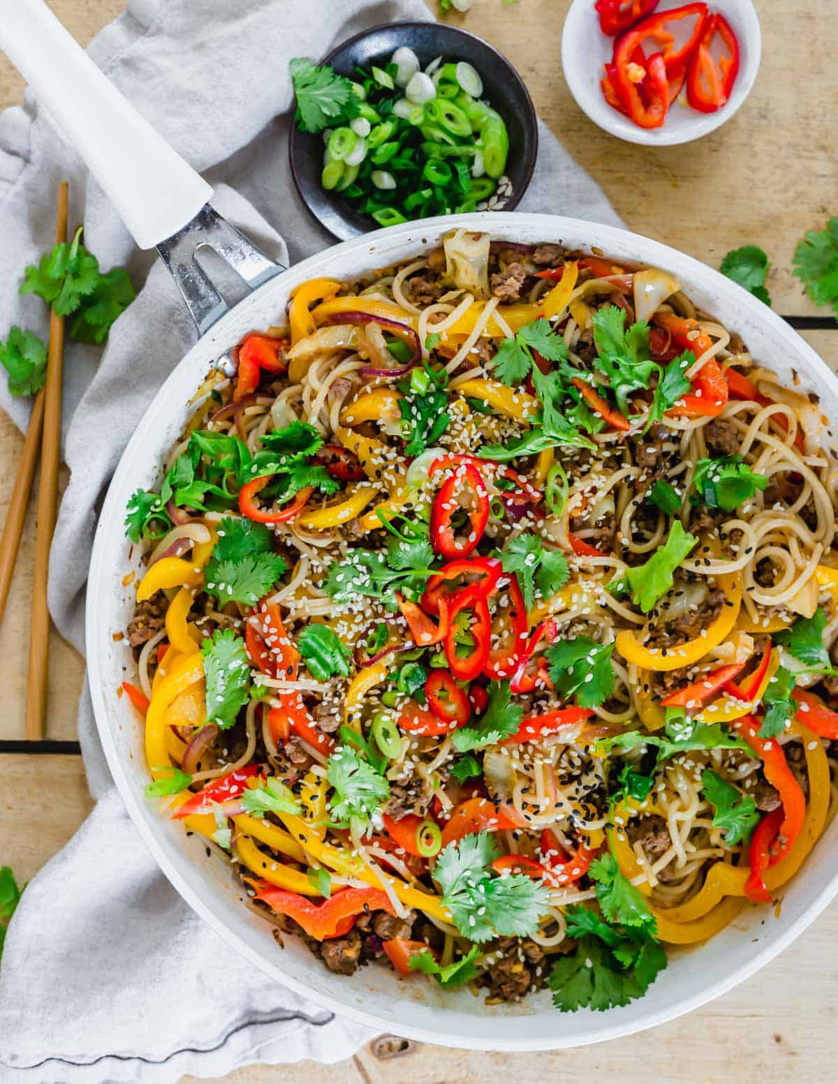 Udon noodle stir fry recipe in a white skillet garnished with sesame seeds and cilantro with chopsticks on the side.