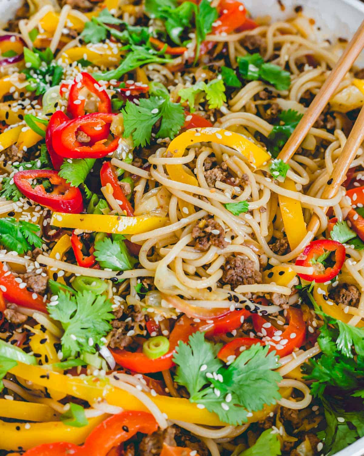 Close up of udon noodles tossed in a spicy sriracha garlic sauce with peppers, scallions and cilantro.