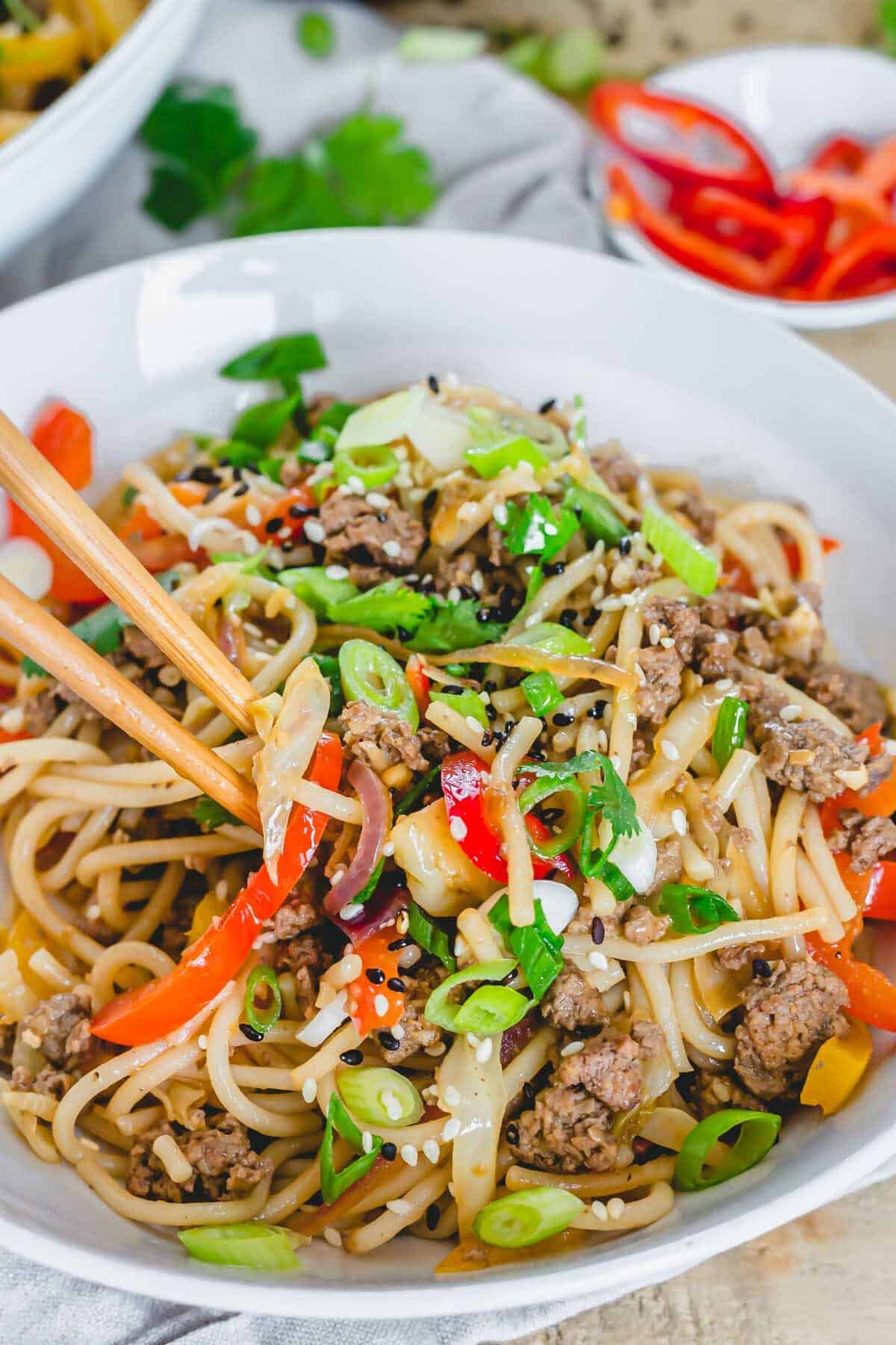 Spicy udon noodles with beef and scallions in a white bowl with chopsticks.