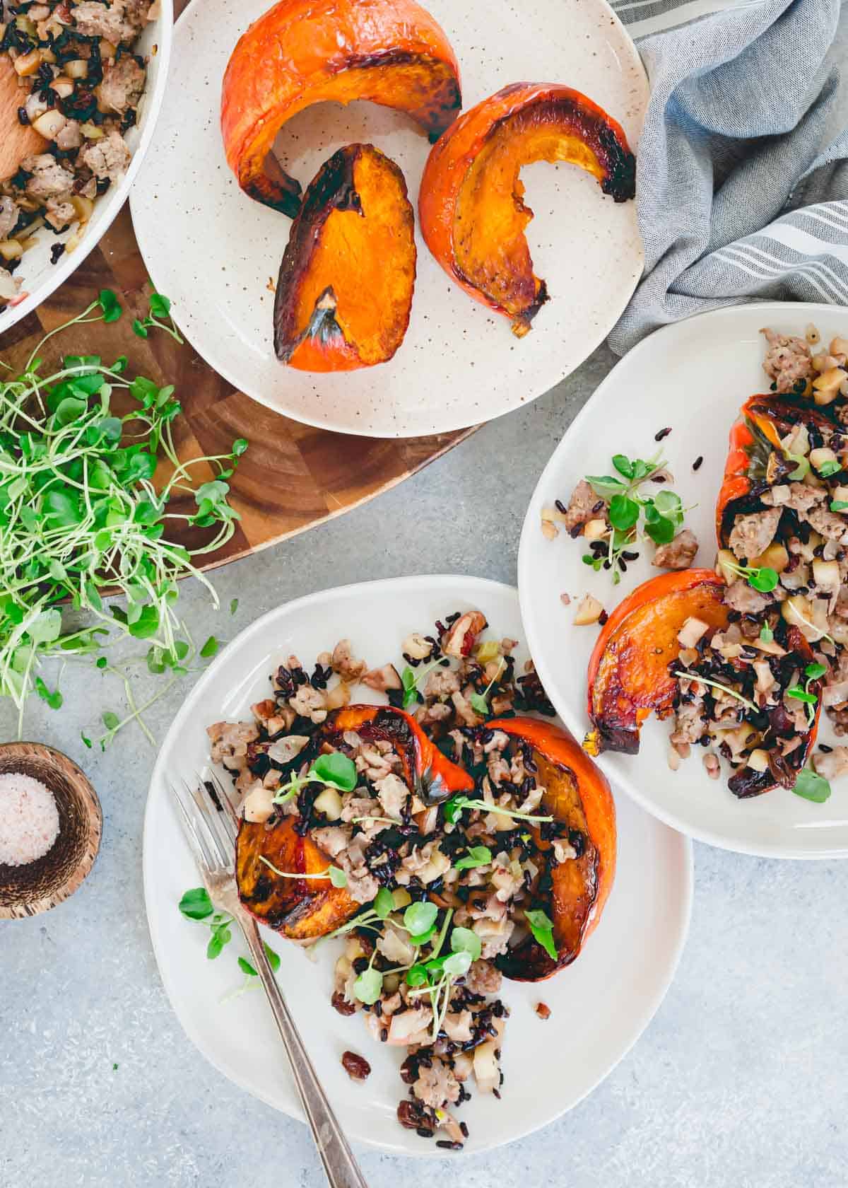 Roasted red kuri squash stuffed with sausage, apples and mushrooms on white plates with microgreens.