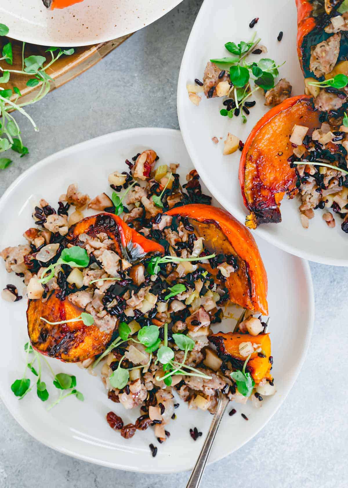 Oven roasted red kuri squash with a fall sausage stuffing garnished with watercress greens on a plate.