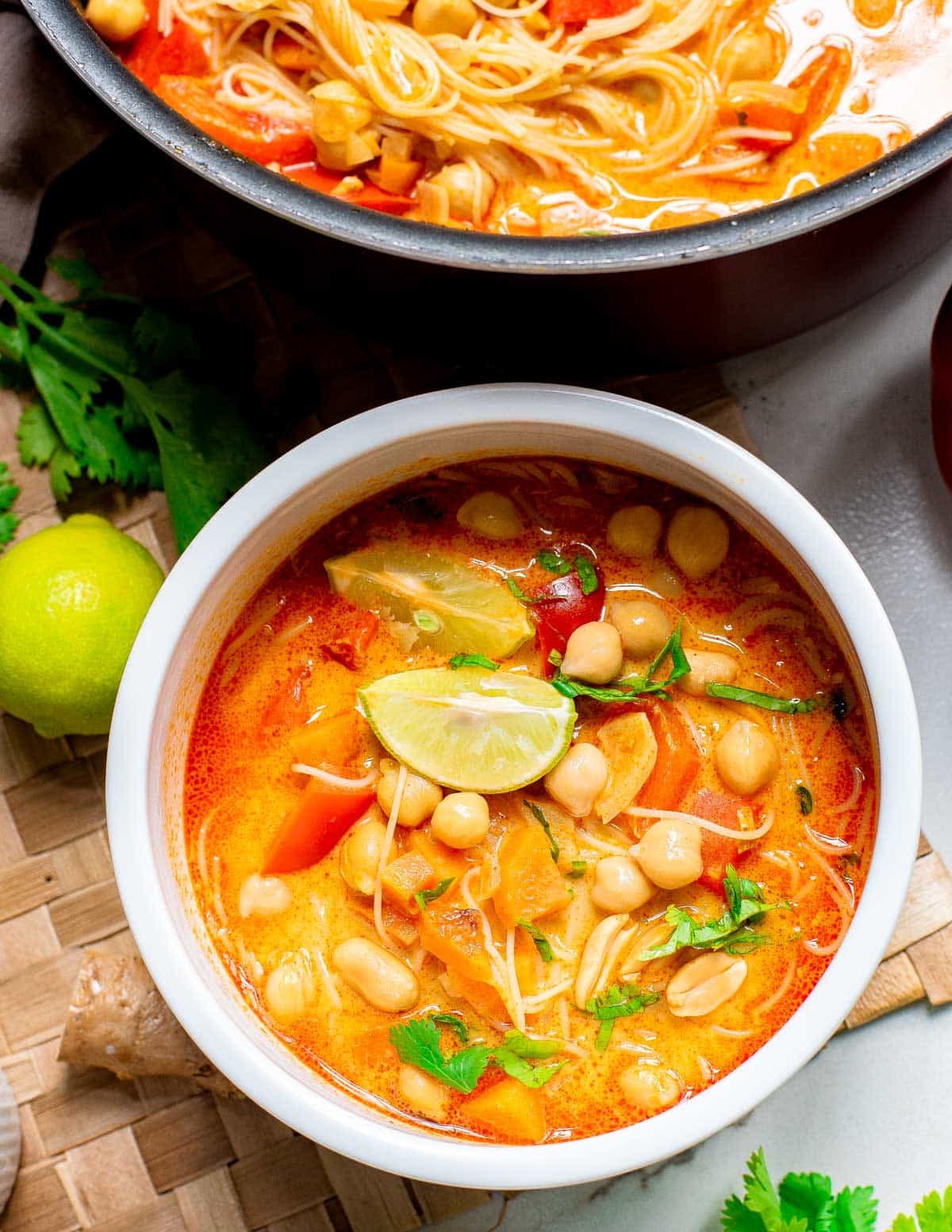 Red curry Thai soup in a white bowl garnished with lime and cilantro on a woven placemat.