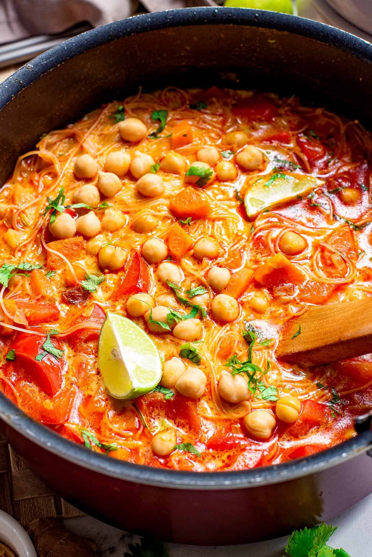 Red curry Thai soup recipe with chickpeas served in a pot with a large wooden spoon.