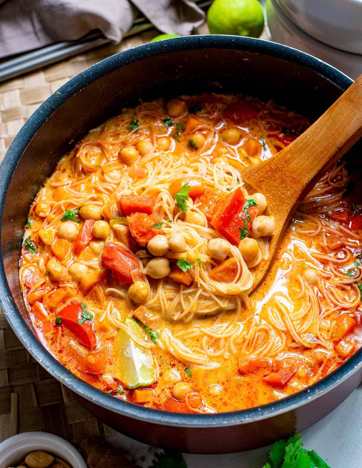 Thai red curry soup in a pot with a wooden spoon.